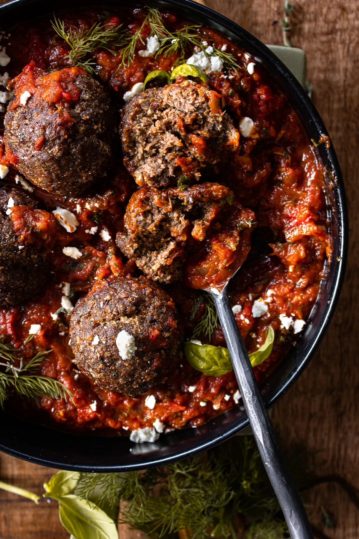 Close overhead view of the meatballs in spicy tomato sauce with a metal serving spoon resting in the skillet