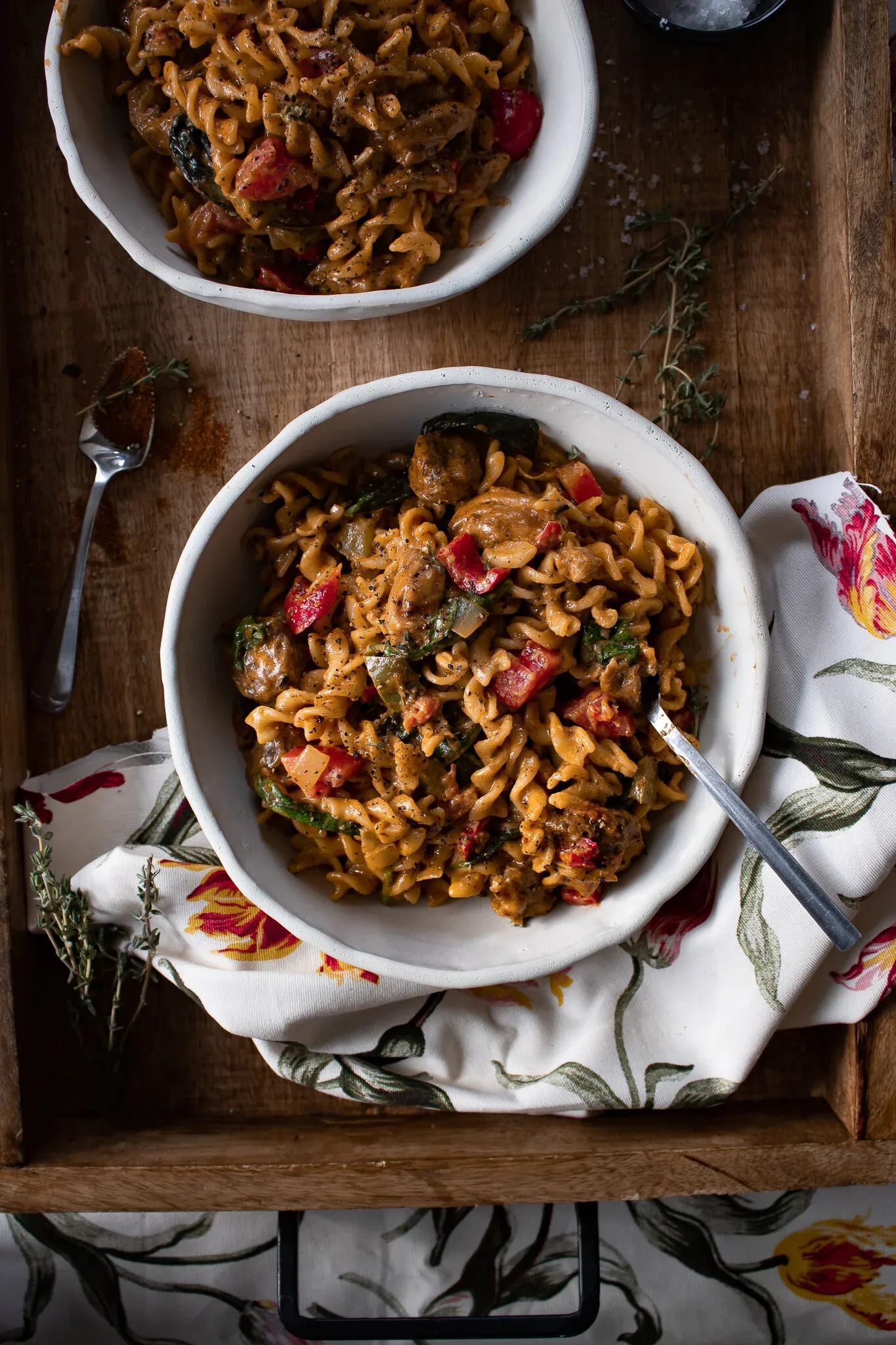 Wider overhead view showing two white bowls of Cajun Chicken and Sausage Pasta on a wood tray