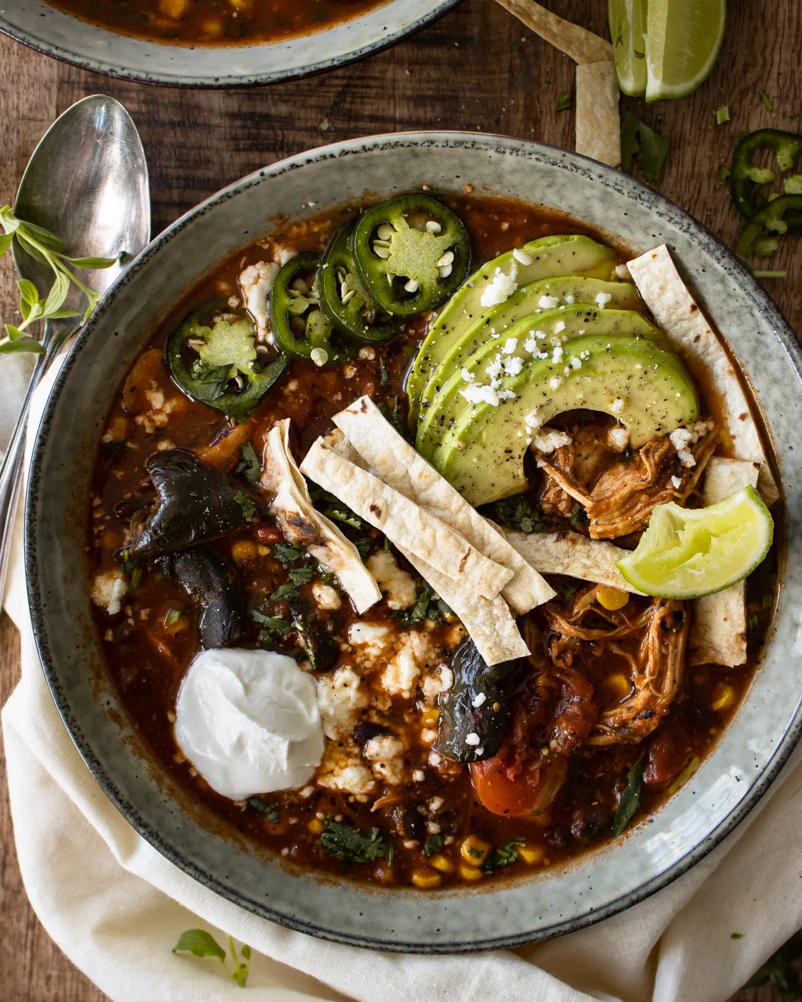 Close overhead view of a single ceramic bowl of Chicken Tortilla Soup showcasing the full garnish arrangement