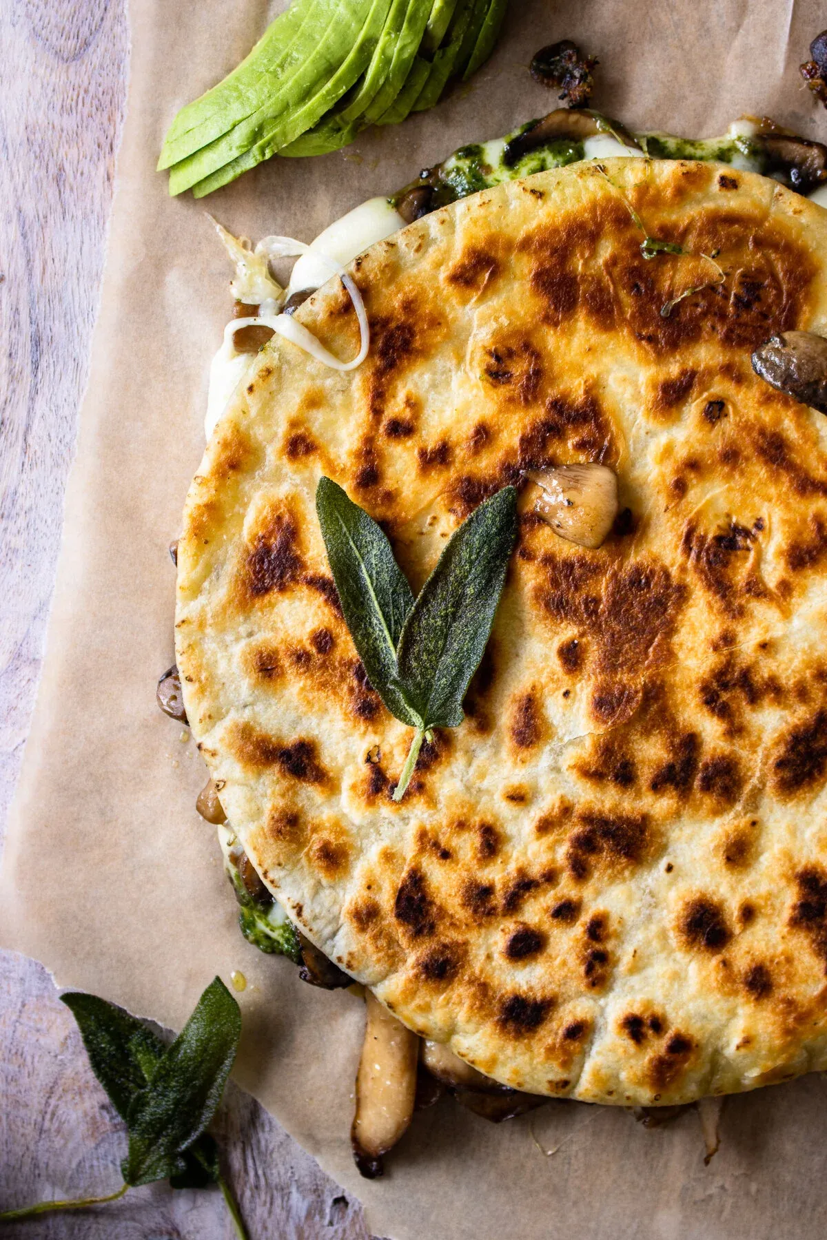 Close overhead angle of the uncut Wild Mushroom and Pesto Quesadilla on parchment showing the upper half of the quesadilla