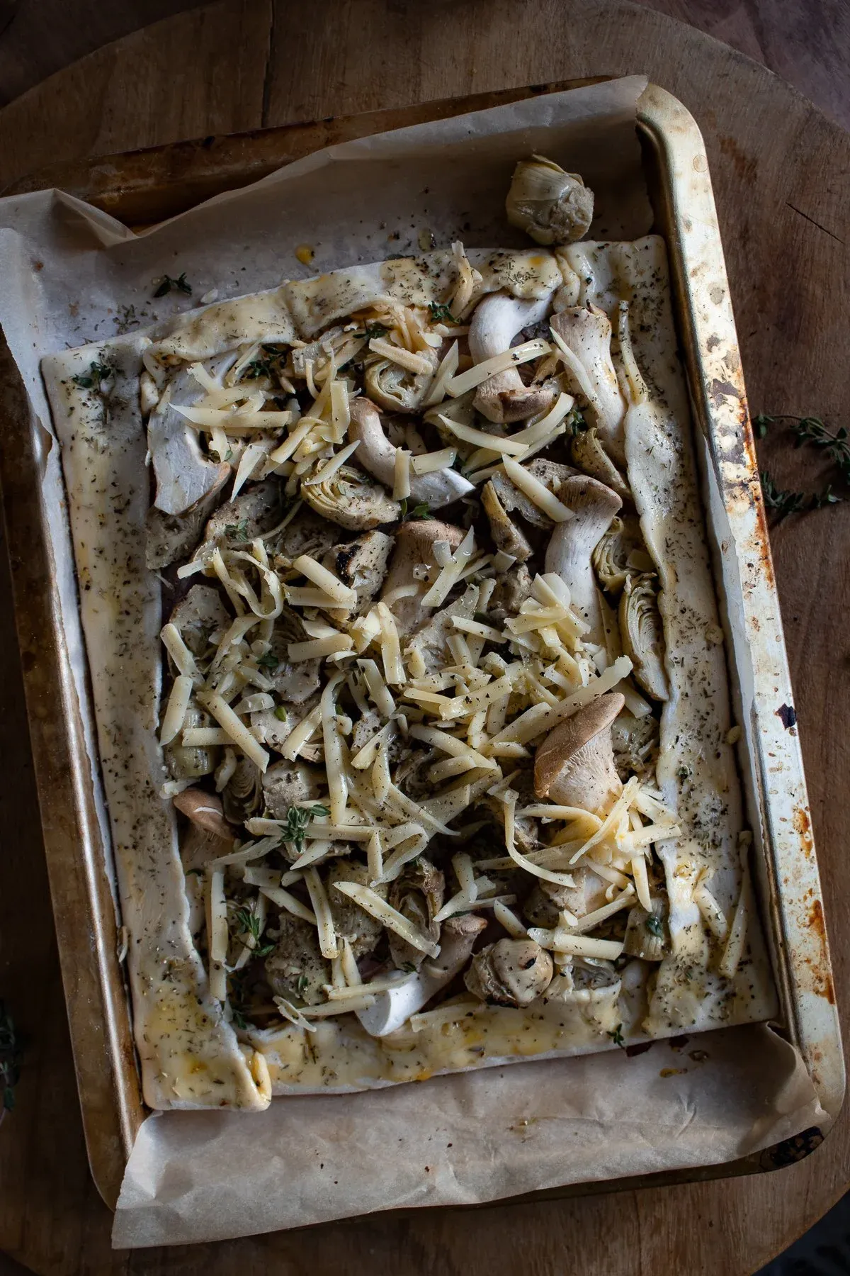Unbaked Artichoke and Mushroom Tart assembled on parchment in a metal baking sheet, with sliced oyster mushrooms