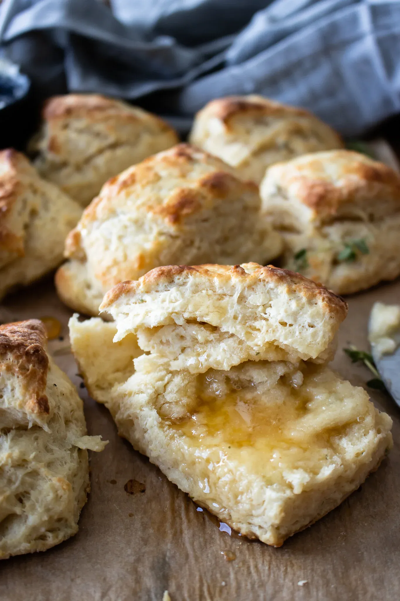 Side shot of a split lemon thyme buttermilk biscuit with liquid honey puddled on the torn interior crumb