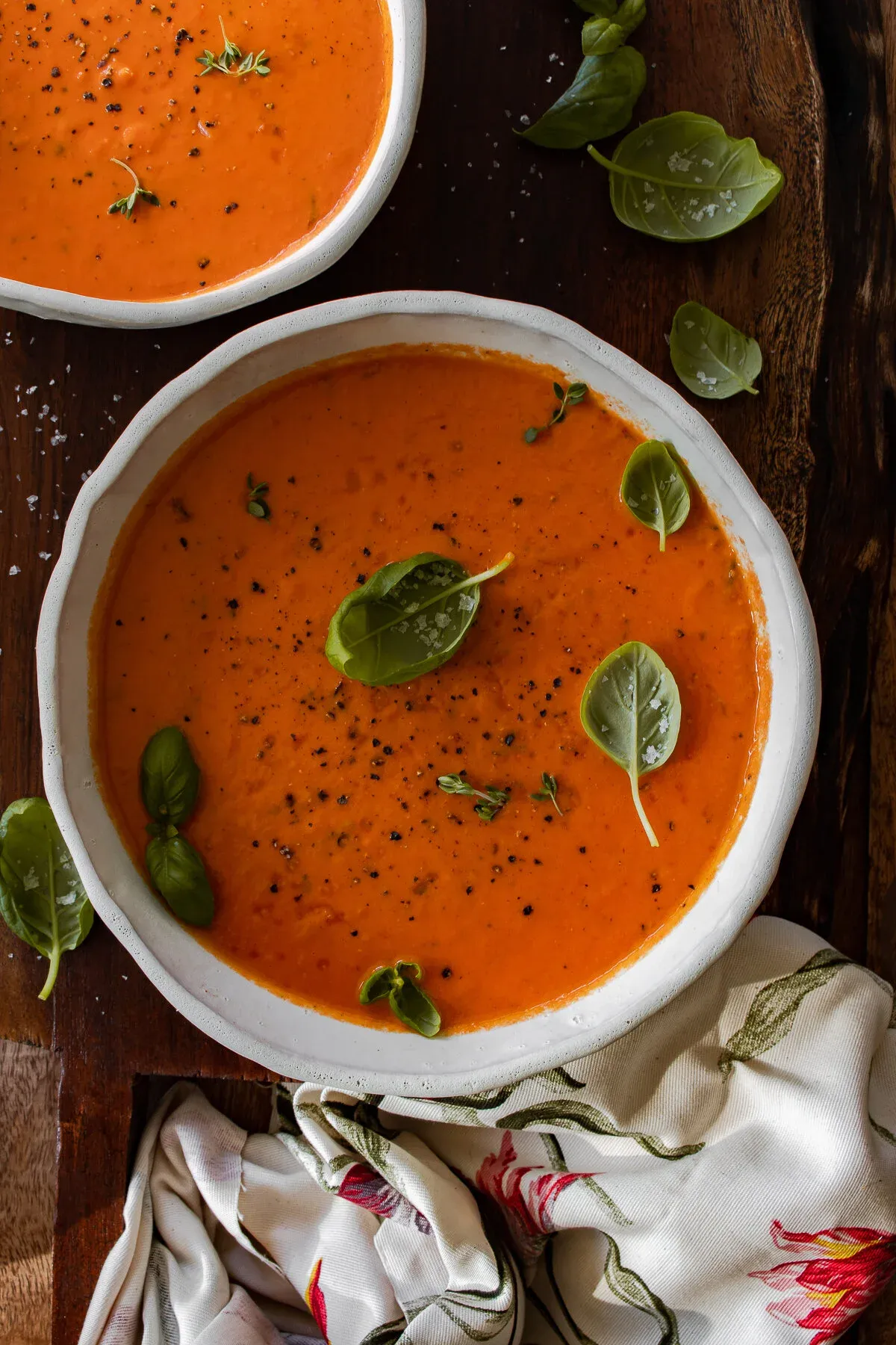 Overhead view of two white ceramic bowls of One Pot Roasted Tomato and Herb Soup on a dark wooden board
