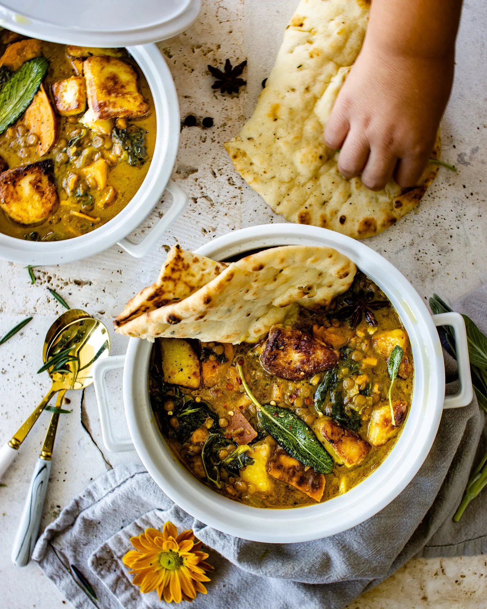 Wider overhead shot of two white ceramic pots of sweet potato and lentil soup with fried halloumi on a textured stone surface