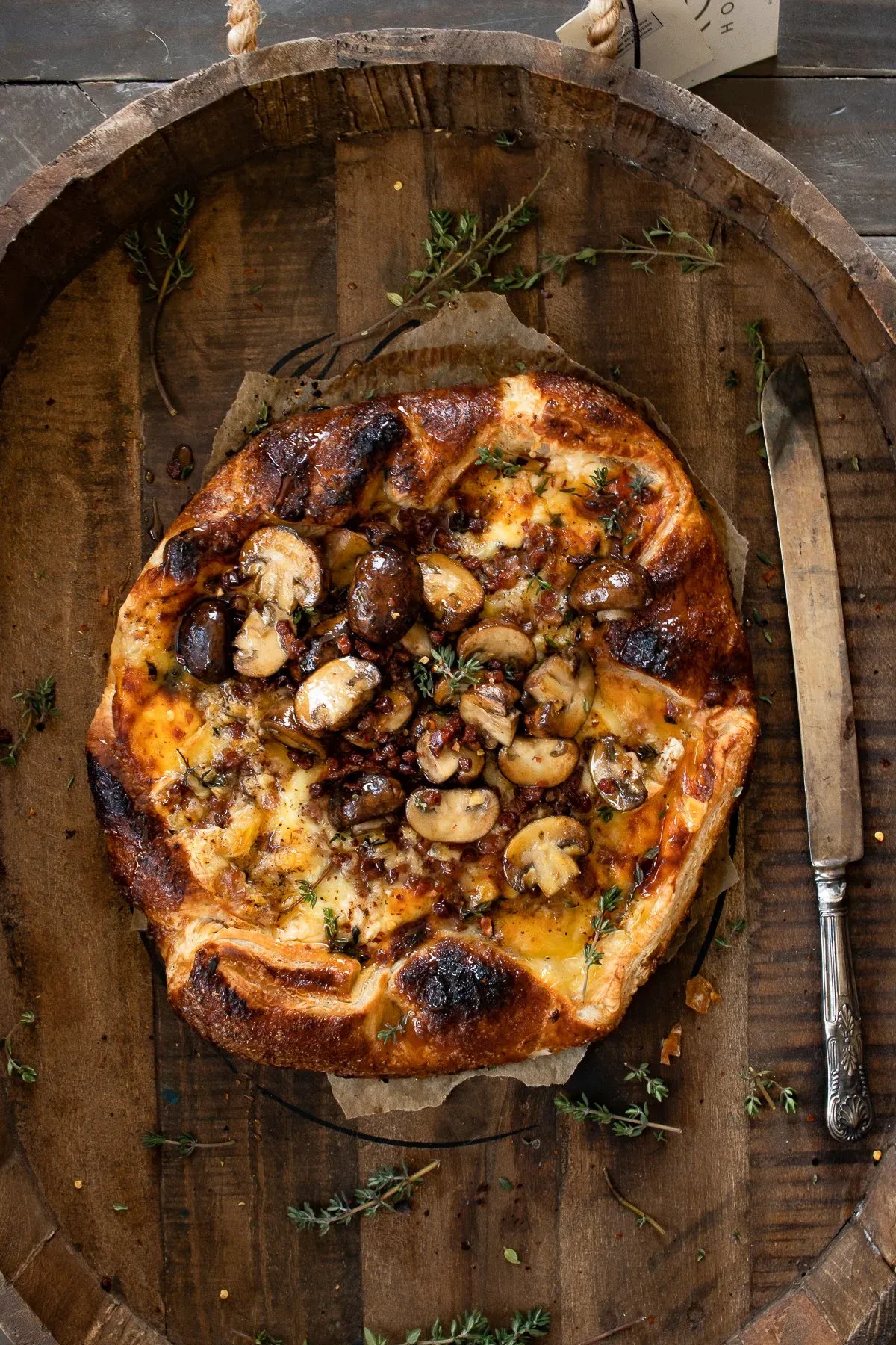 Overhead shot of a whole puff pastry wrapped brie with pancetta and mushrooms inside a round barrel-wood tray on a rustic wood surface