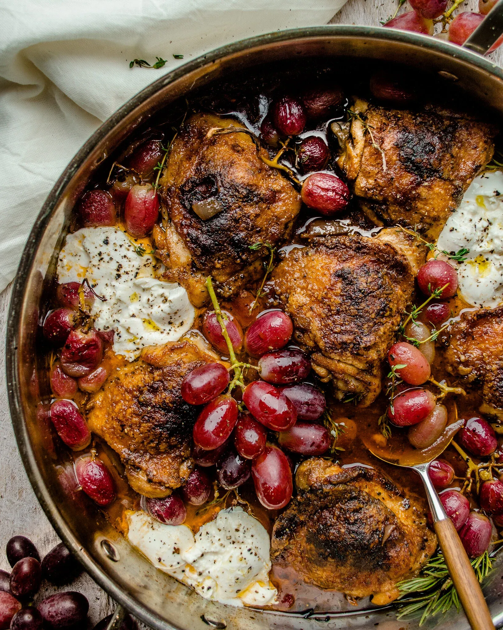 Wide overhead shot of red wine balsamic braised chicken thighs with grapes and burrata in a stainless skillet