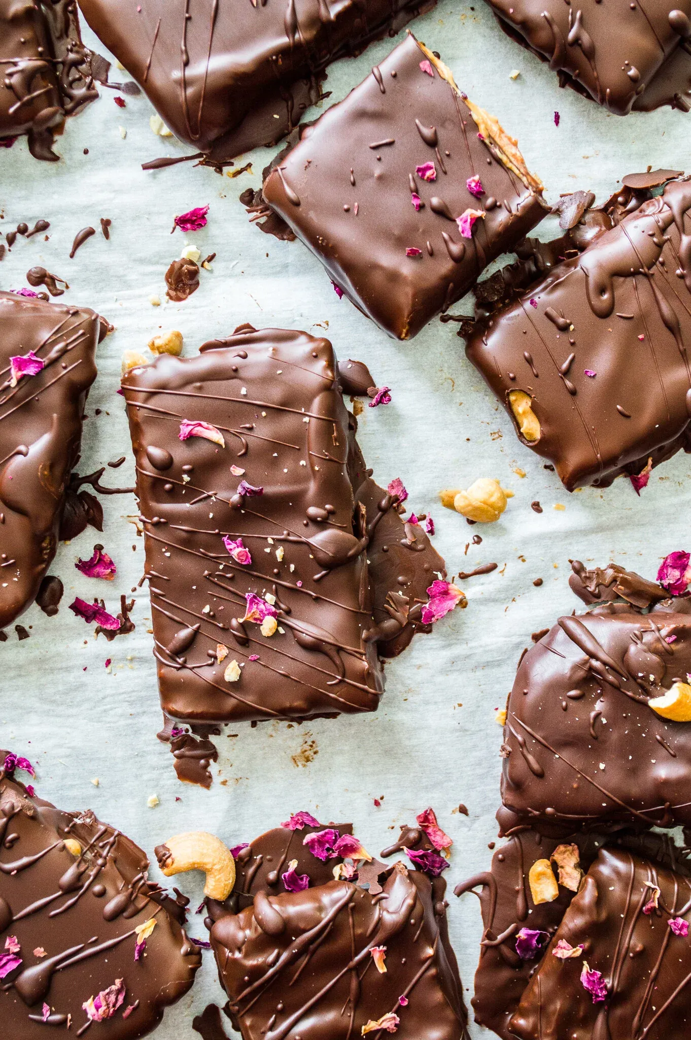 Overhead flat-lay of eight No Bake Dark Chocolate Nut Butter Bars scattered on white parchment paper