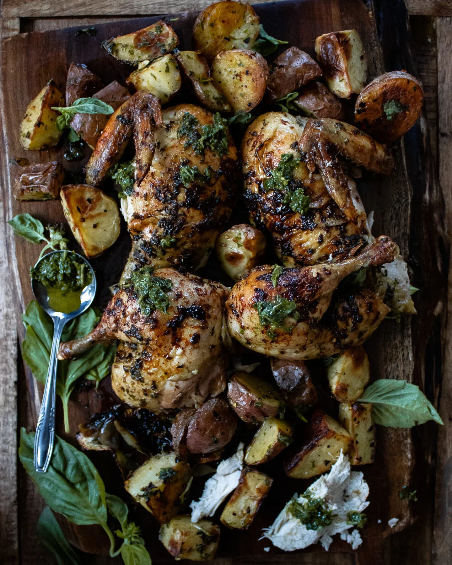 Overhead shot of two spatchcocked grilled chickens with charred herb-coated skin on a rustic wooden plank