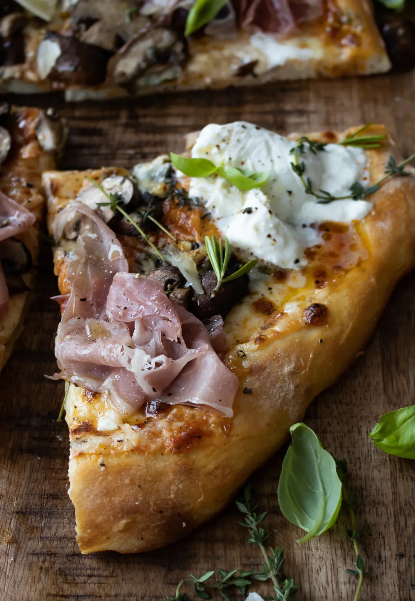 A single wedge slice of Roasted Mushroom and Prosciutto Pizza on a wooden board