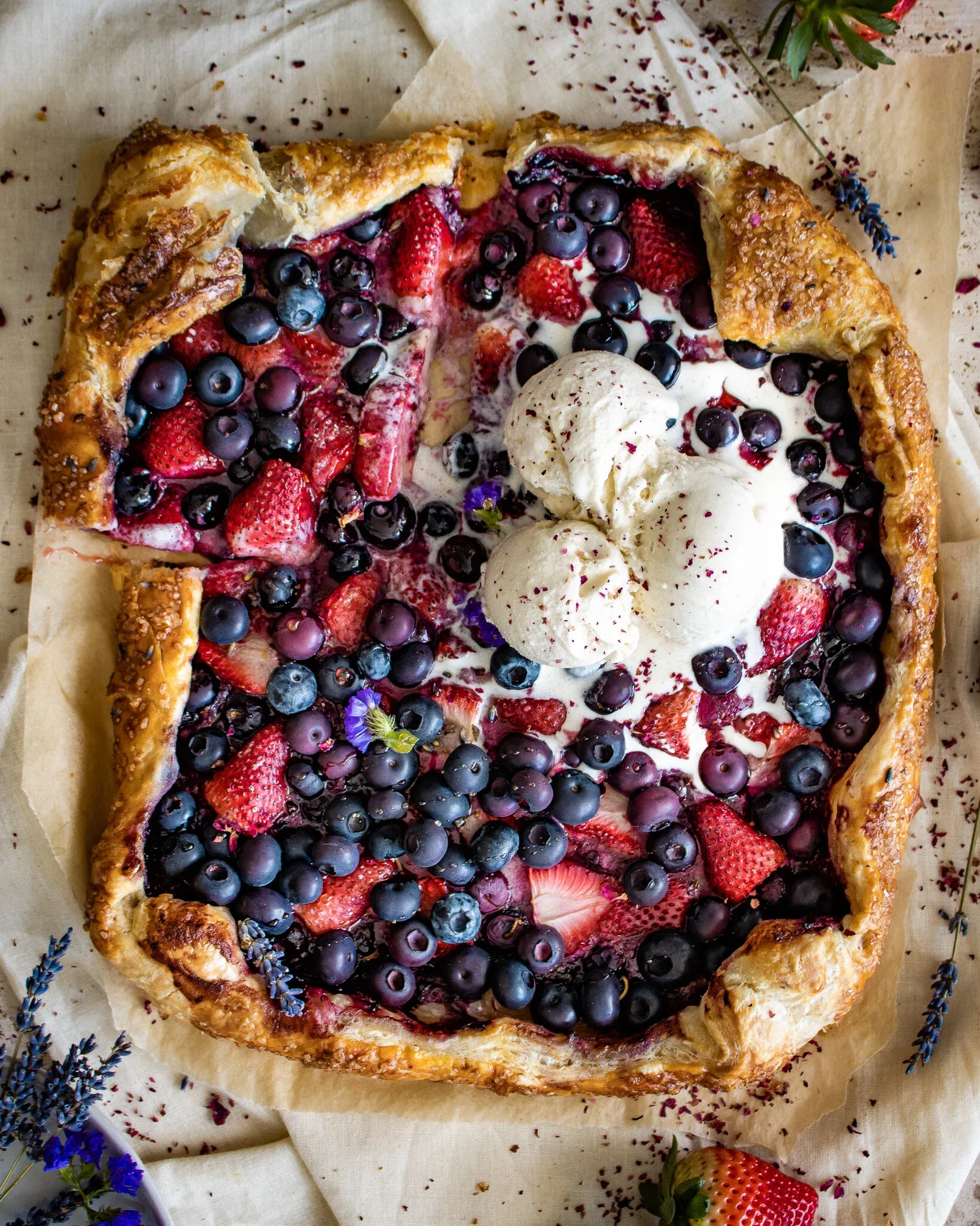 Overhead view of the puff pastry berry galette served with two generous scoops of vanilla ice cream melting into the warm dark berry filling