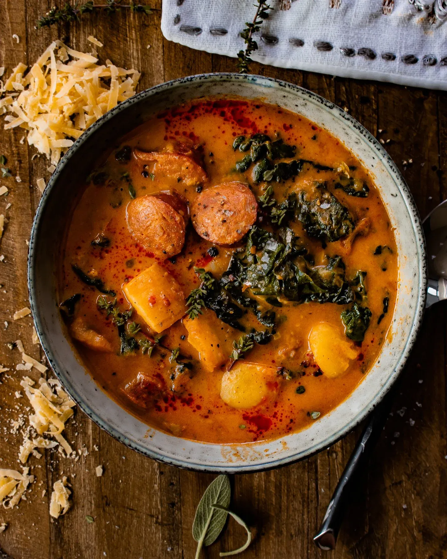 Smoked Potato and Sausage Soup in a speckled grey ceramic bowl, top-down view on a dark wooden surface