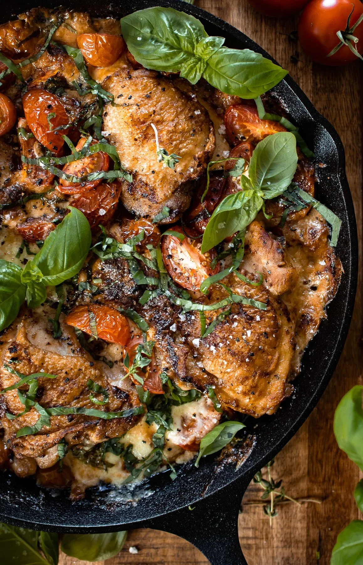 Angled close-up of cast iron caprese chicken thighs from slightly
