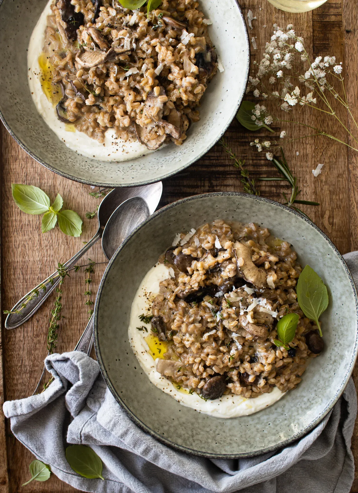Overhead flat-lay showing both grey stoneware bowls of Farro Risotto with Mushrooms side by side on a rustic wood surface
