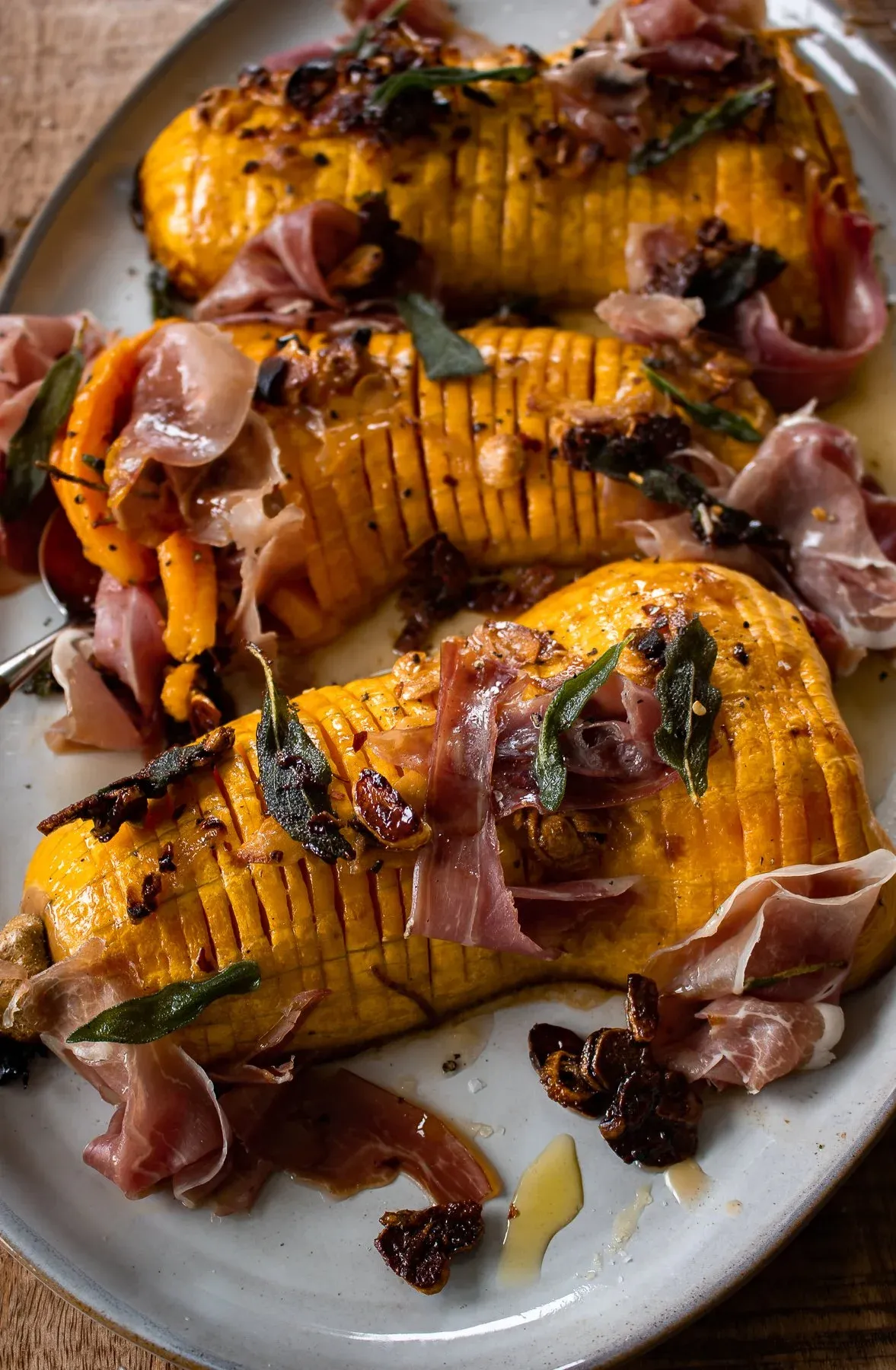 Angled close-up of two caramelized hasselback butternut squash halves on a white ceramic platter