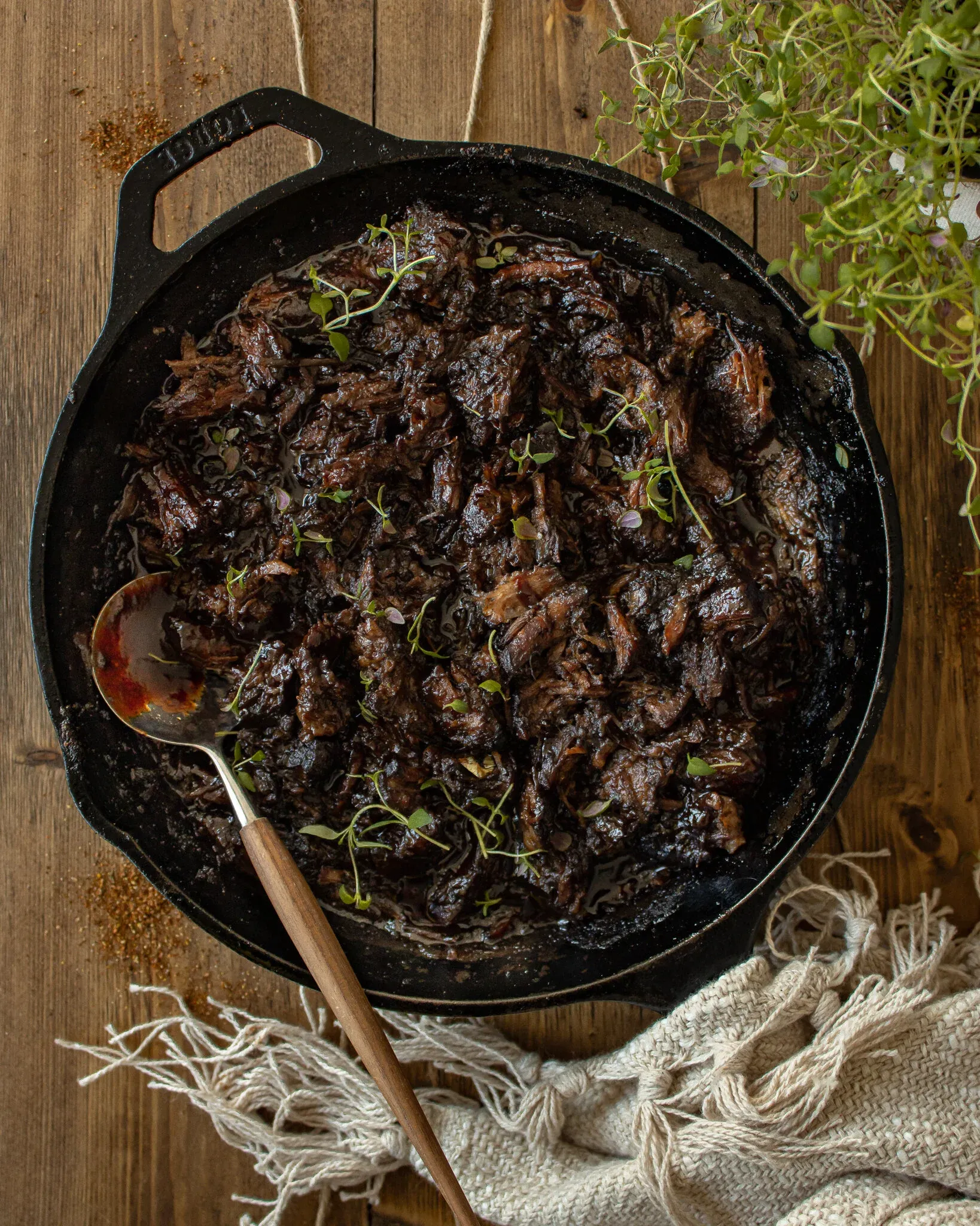 Overhead view of saucy, deeply caramelized BBQ shredded beef filling a large black Lodge cast iron skillet