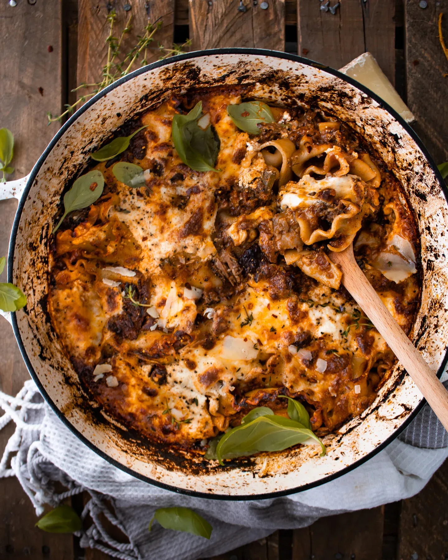 Short Rib Skillet Lasagna being served with a wooden spoon in a white enamel braiser, overhead view