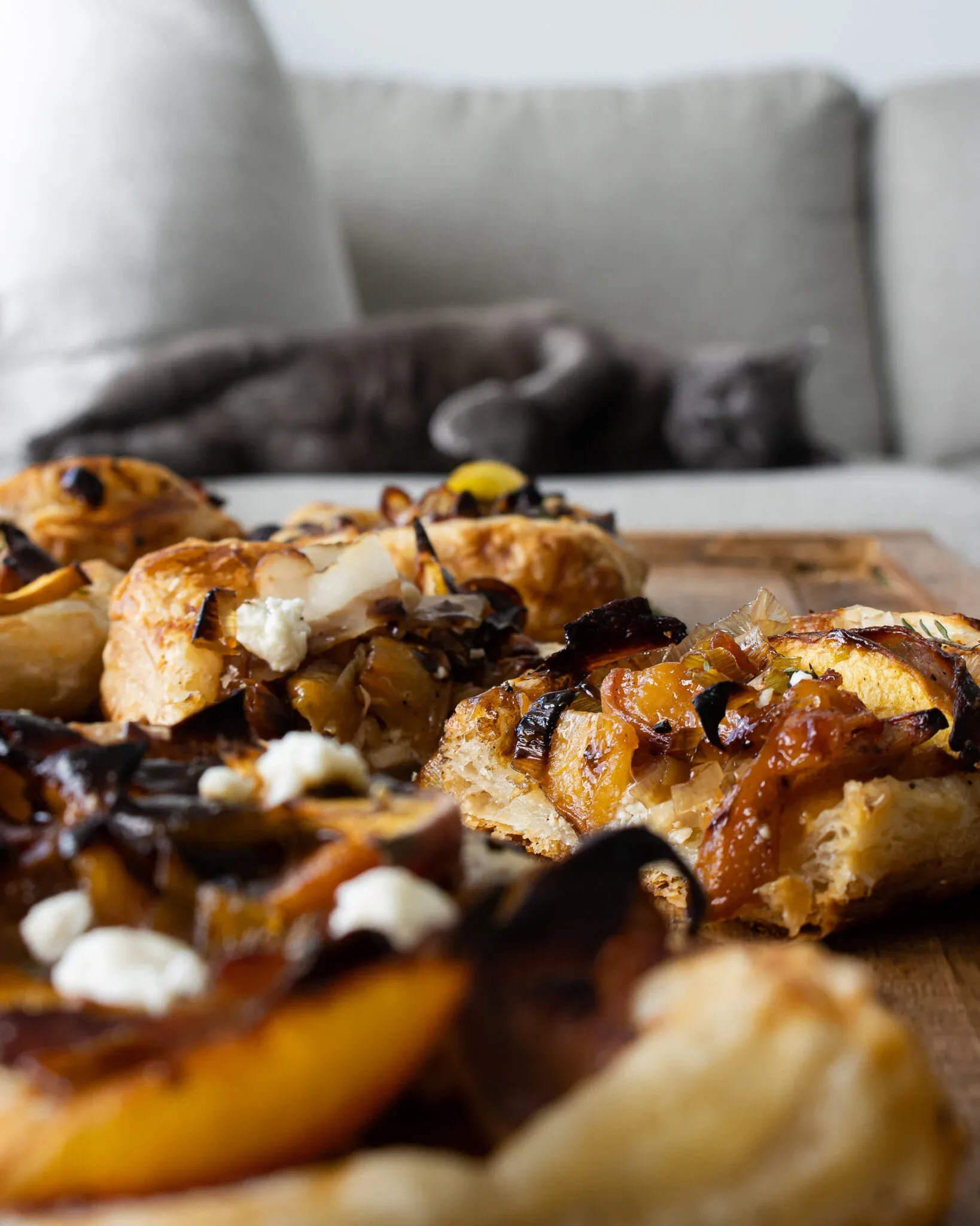 Eye-level close-up of two caramelized leek and peach puff pastry tarts on a wooden board showing the flaky laminated pastry layers in sharp detail