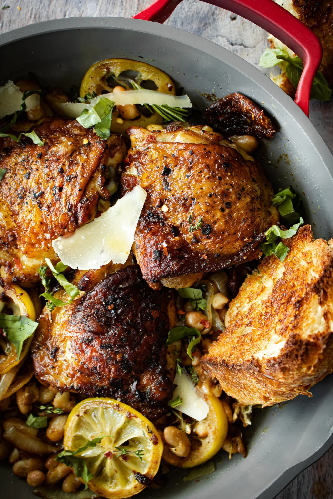 Angled close-up of three deeply charred oven-roasted chicken thighs in the gray braiser