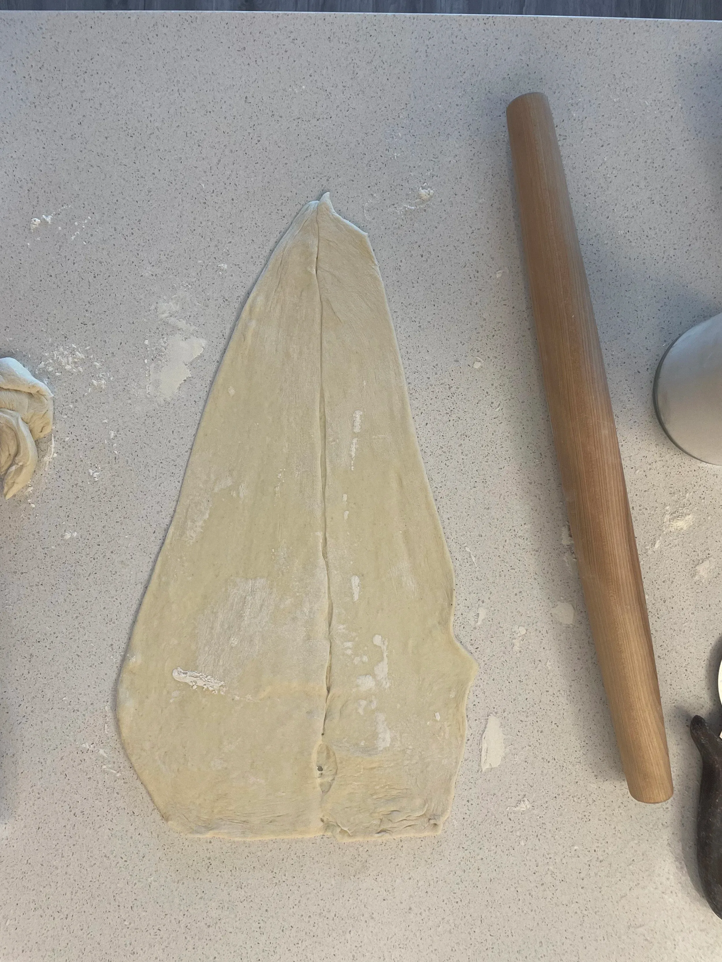 Process shot showing raw bread dough hand-stretched and rolled into a tall triangular Christmas tree shape on a lightly floured light gray granite counter
