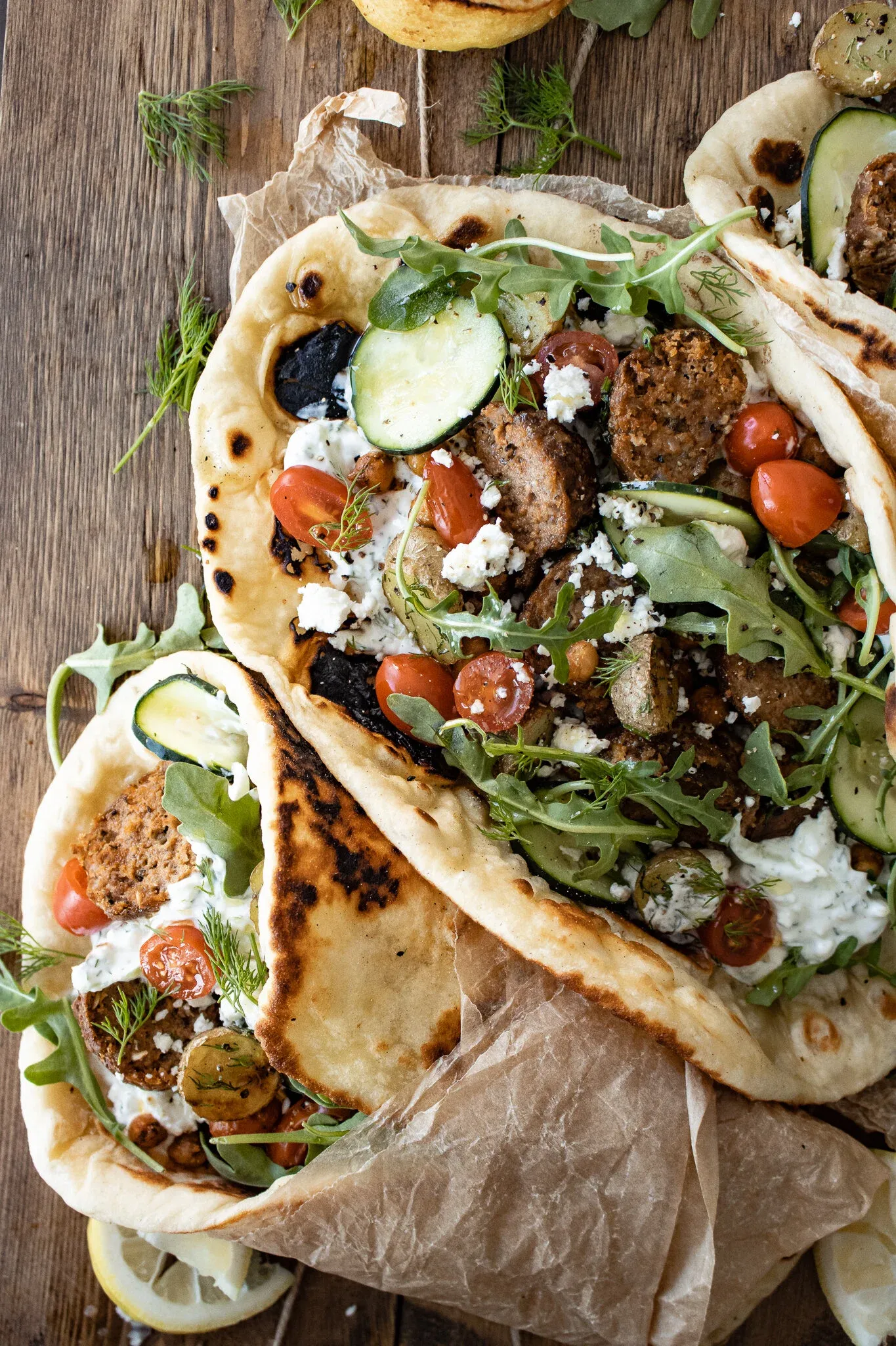 Close overhead shot of two charred flatbread lamb wraps stacked on parchment paper, loaded with herb-spiced lamb chunks