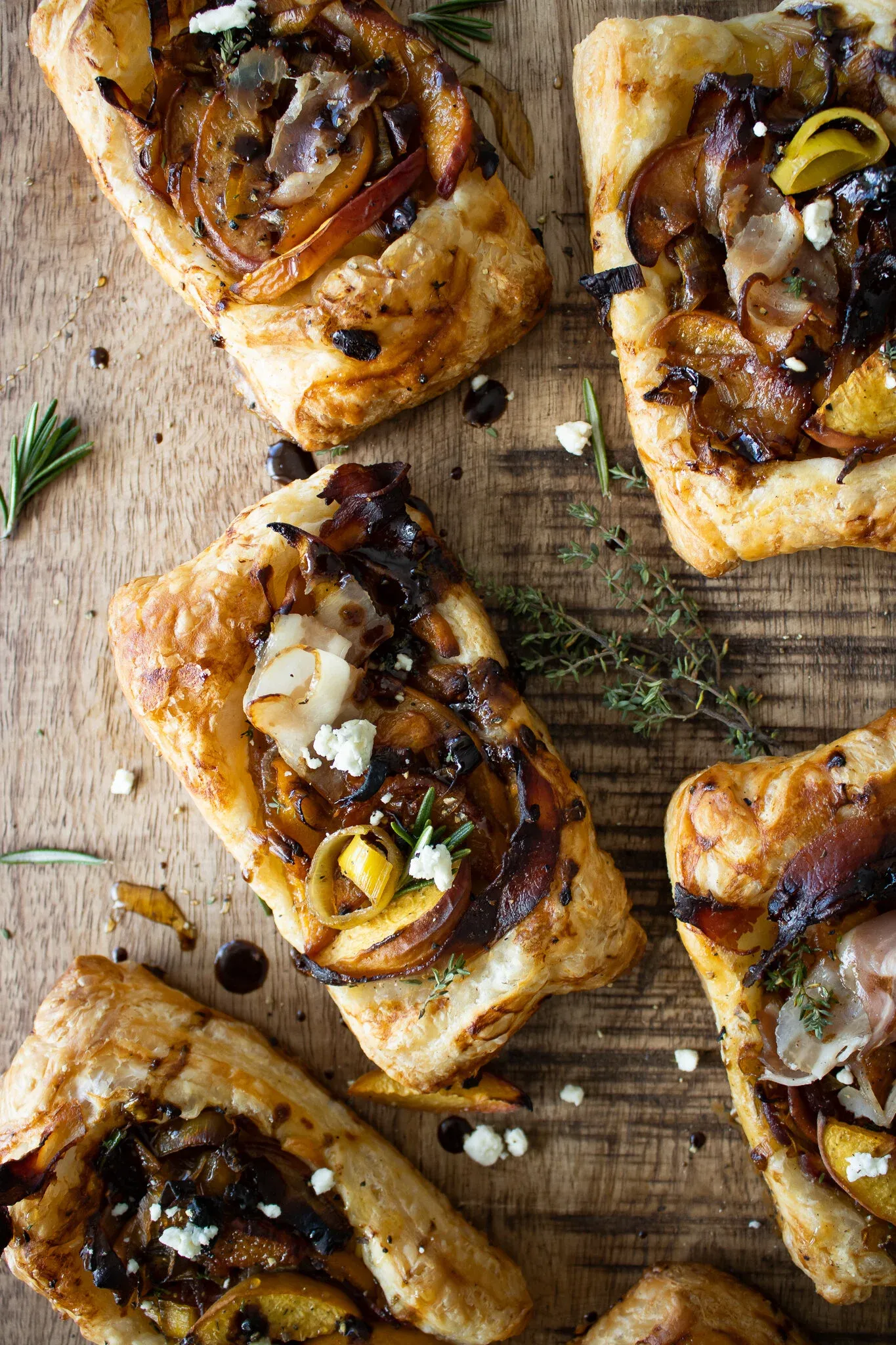 Overhead shot of five caramelized leek and peach puff pastry tarts arranged on a rustic wooden cutting board