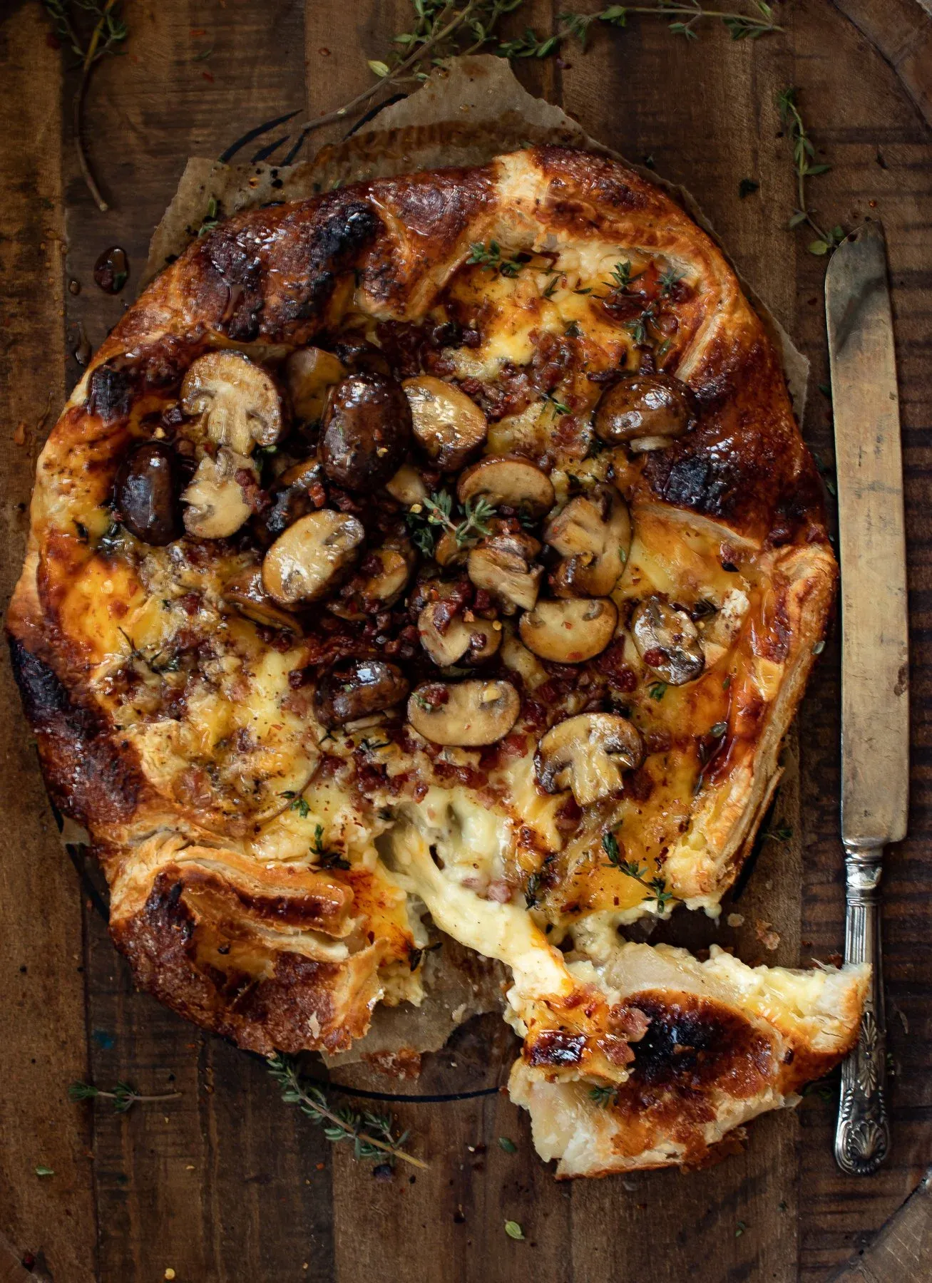Angled overhead view of the puff pastry wrapped brie with pancetta and mushrooms with a slice broken off at the bottom