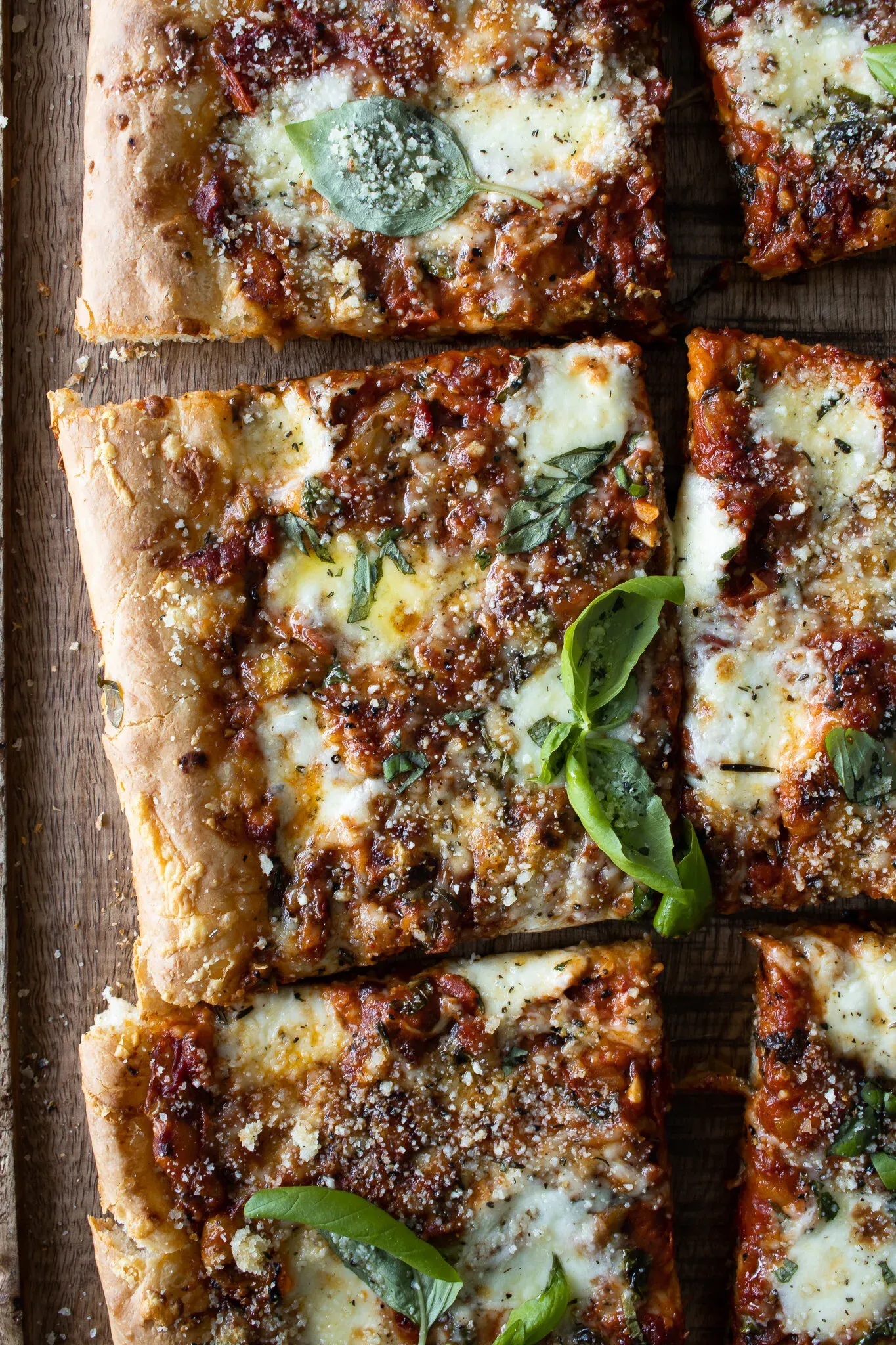 Close-up overhead shot of three rows of Sicilian-inspired sheet pan pizza slices on a wooden board