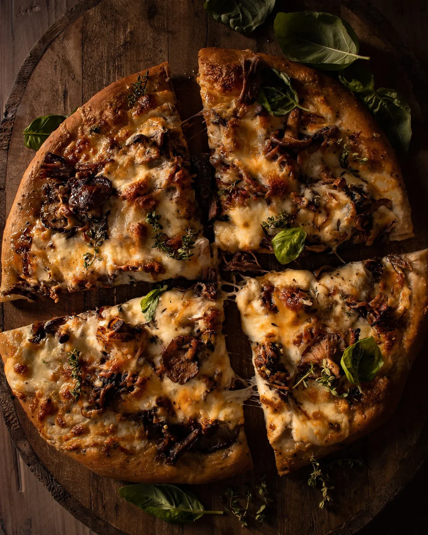 Short Rib and Mushroom Pizza sliced into six wedges on a round wooden board, overhead view showing golden bubbly mozzarella