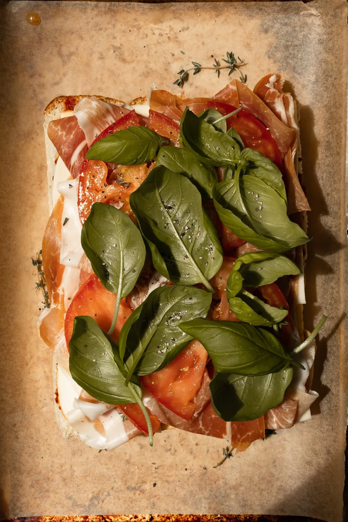 Assembly overhead shot of the slider base on a parchment-lined baking sheet showing layered toppings
