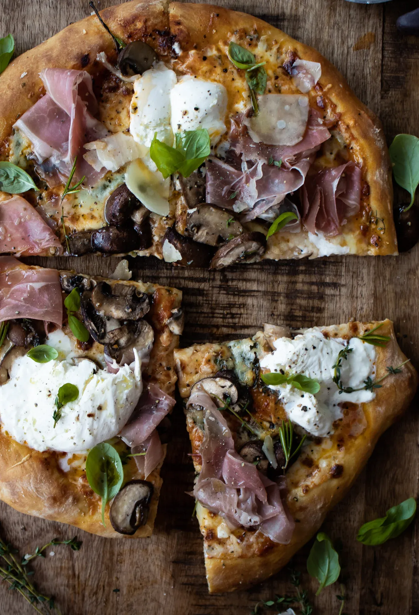 Overhead view of the Roasted Mushroom and Prosciutto Pizza partially sliced on a wooden board