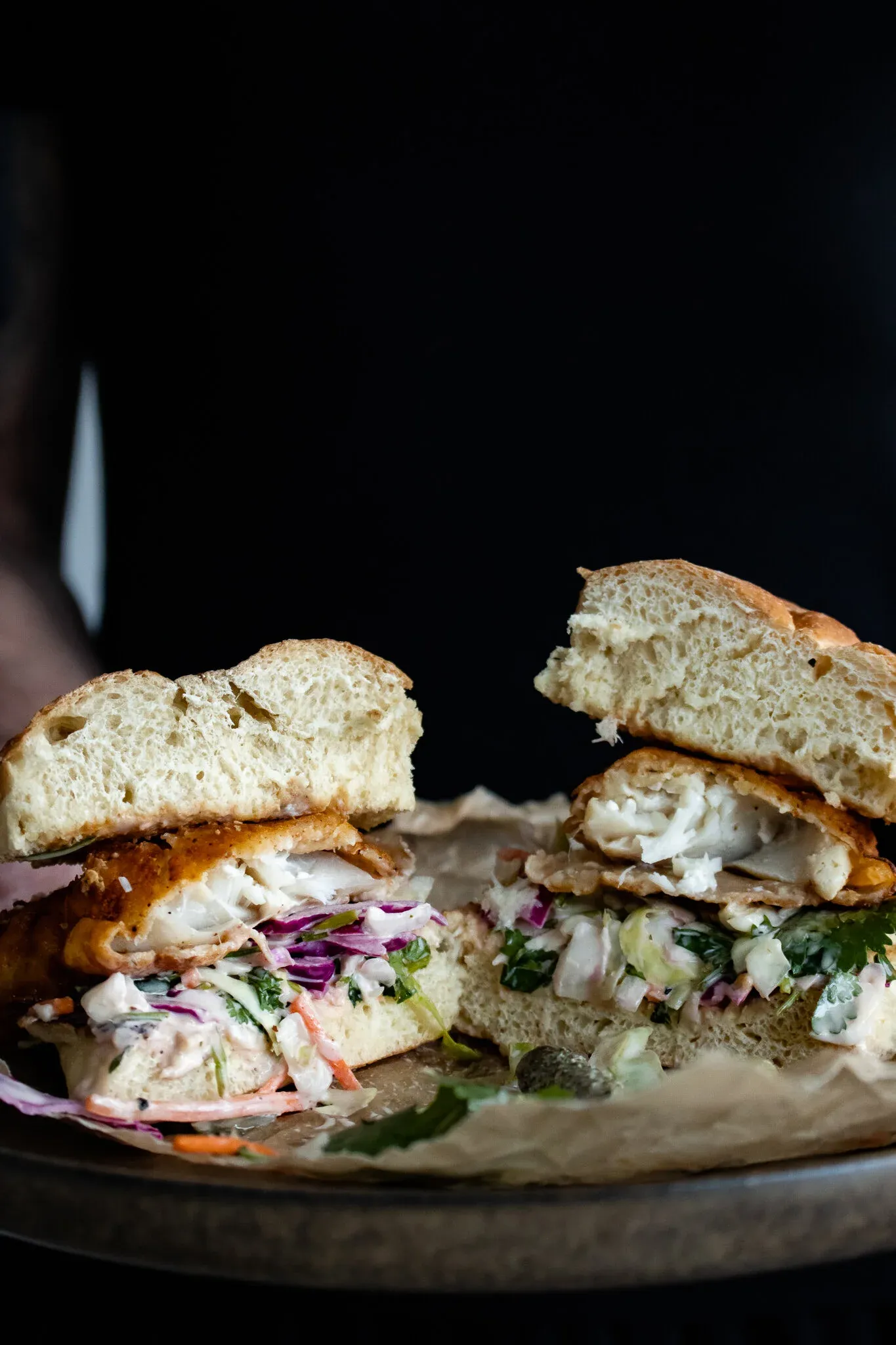 A fried fish sandwich sliced clean in half and pulled apart to reveal flaky white cod inside a crisp golden batter