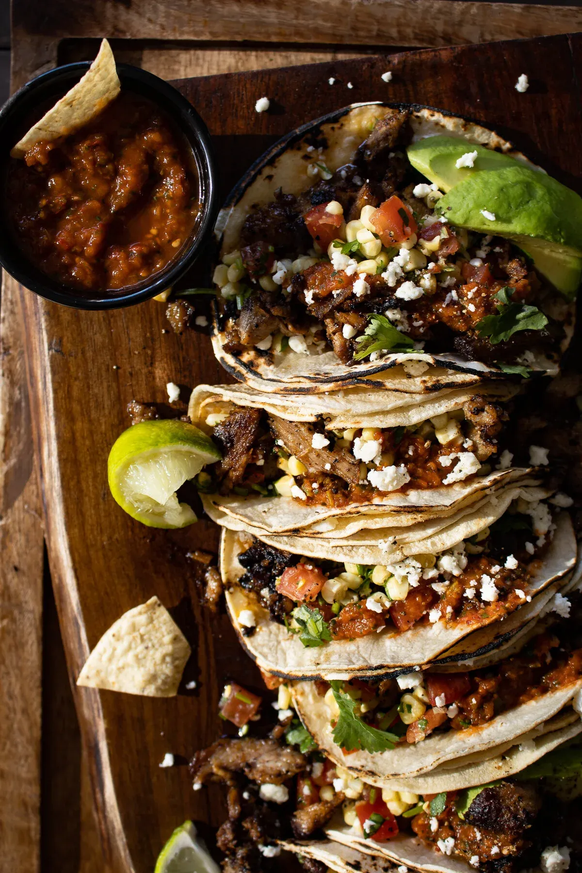 Overhead angled shot of four pernil tacos on the dark wood board