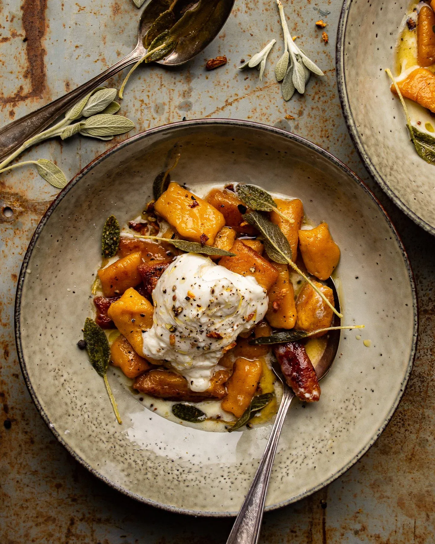 Overhead view of one full bowl of kabocha squash gnocchi with burrata on an aged rust-toned metal surface