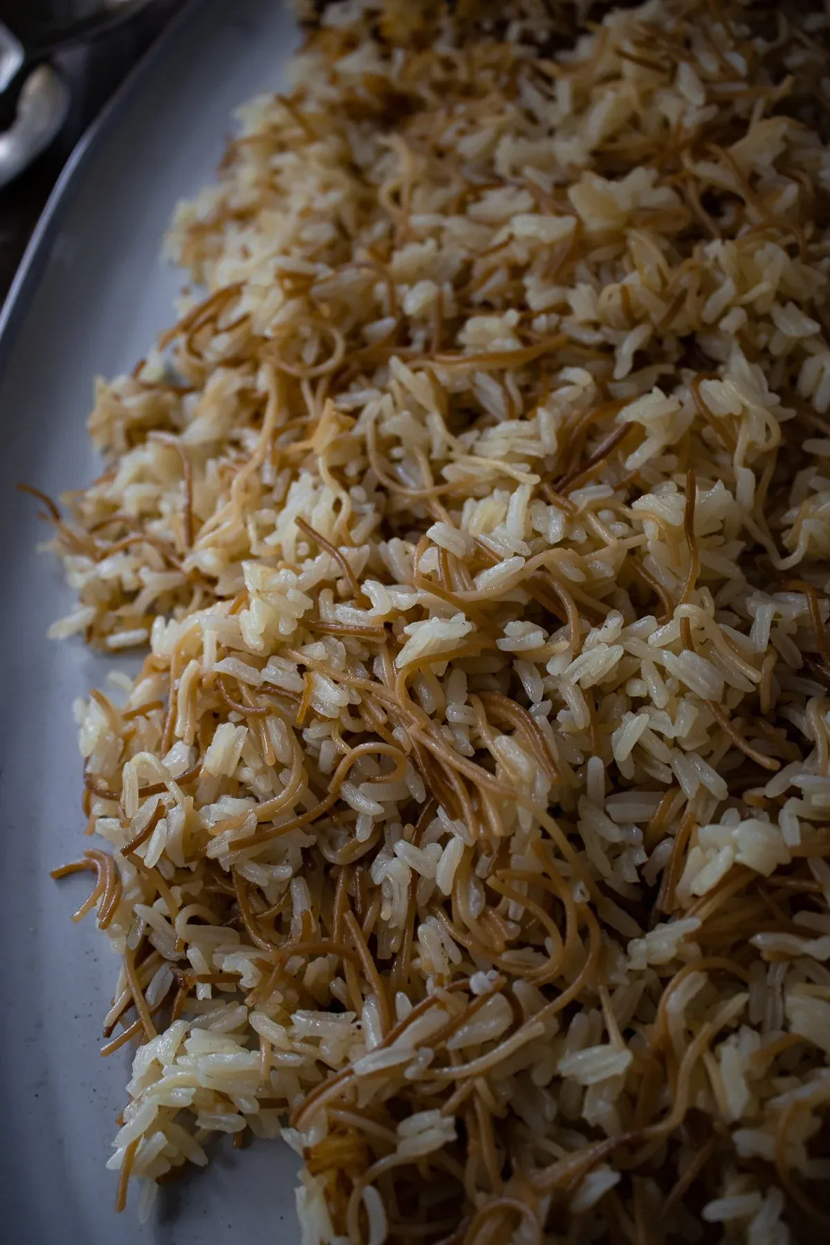 Close-up angled shot of Arroz con Fideos on a grey platter showing the intricate texture of crispy golden-brown fried fideos noodles woven through tender fluffy white rice grains