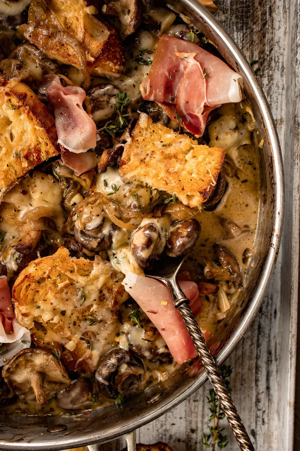 Angled close-up of French Onion Mushrooms in a stainless skillet with a vintage silver ladle resting inside