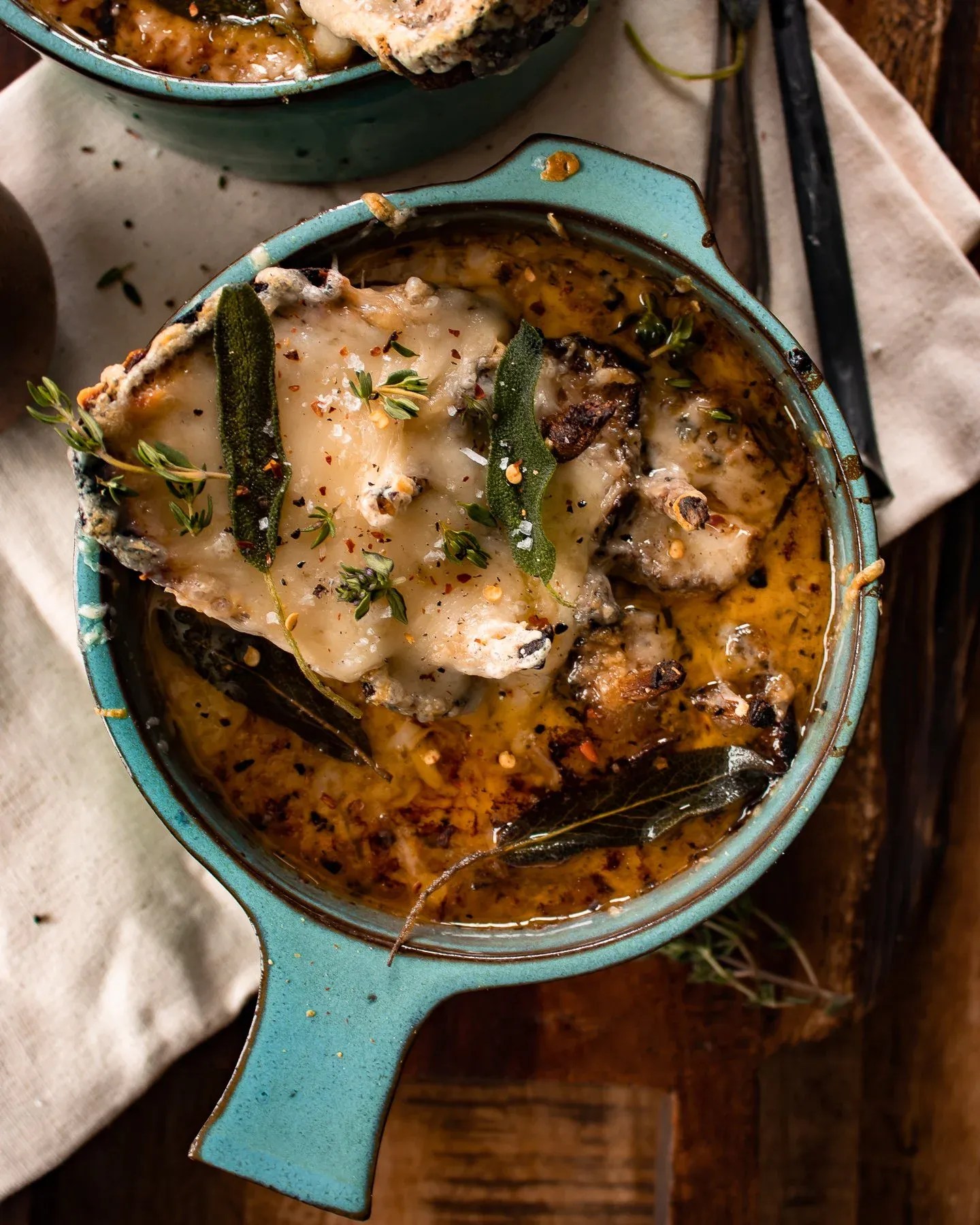Angled overhead close-up of a single teal crock of French Onion and Shallot Soup with Roasted Mushrooms