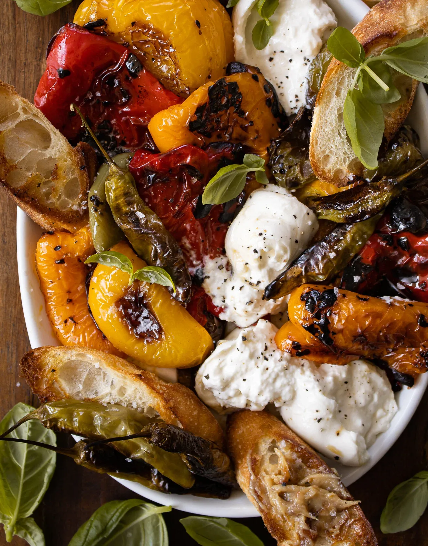 Tight overhead close-up of the roasted pepper and burrata platter showing the caramelized and blackened edges on orange, red