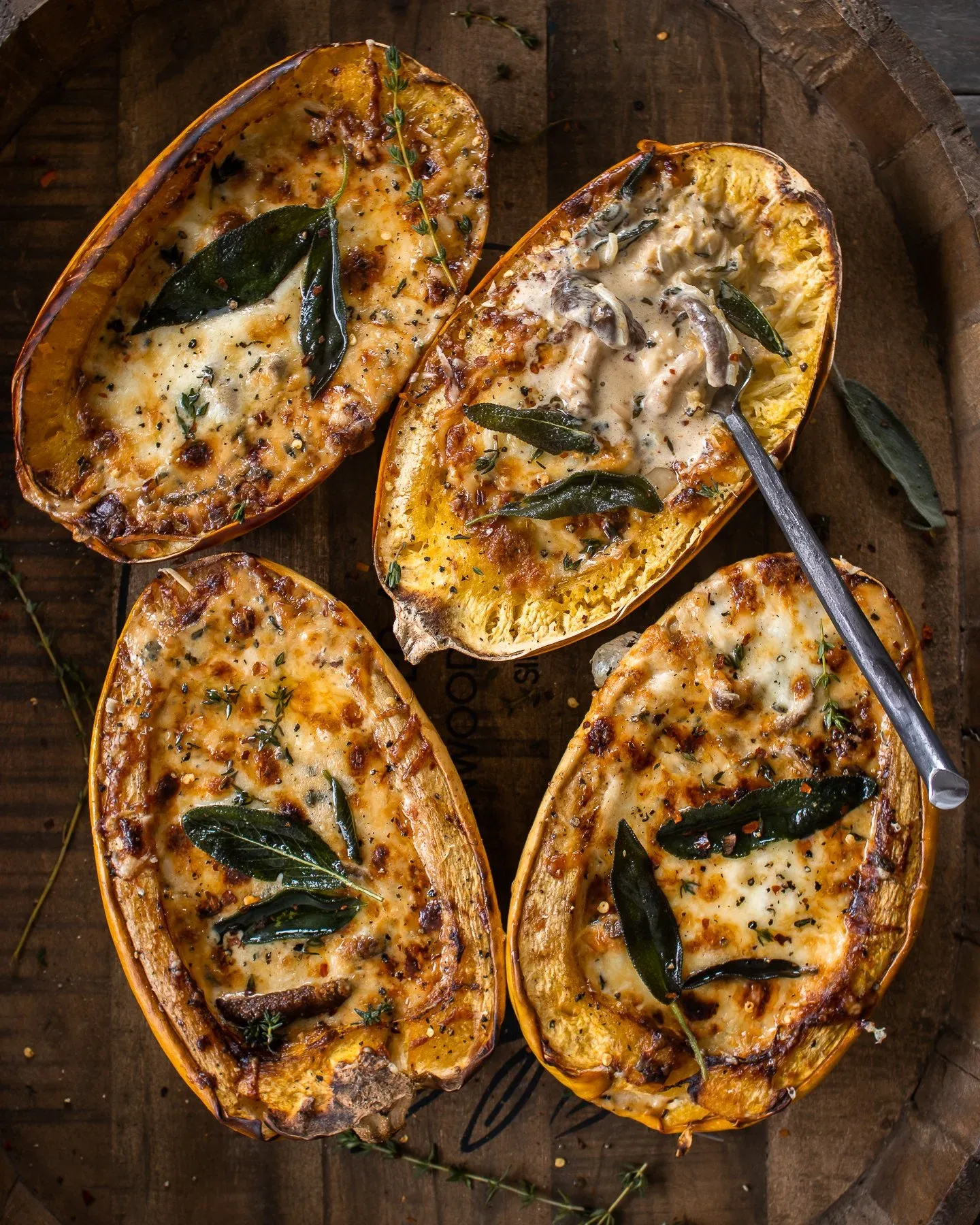 Overhead flat-lay of four Mushroom and Sage Cream Stuffed Spaghetti Squash halves on a wooden barrel tray