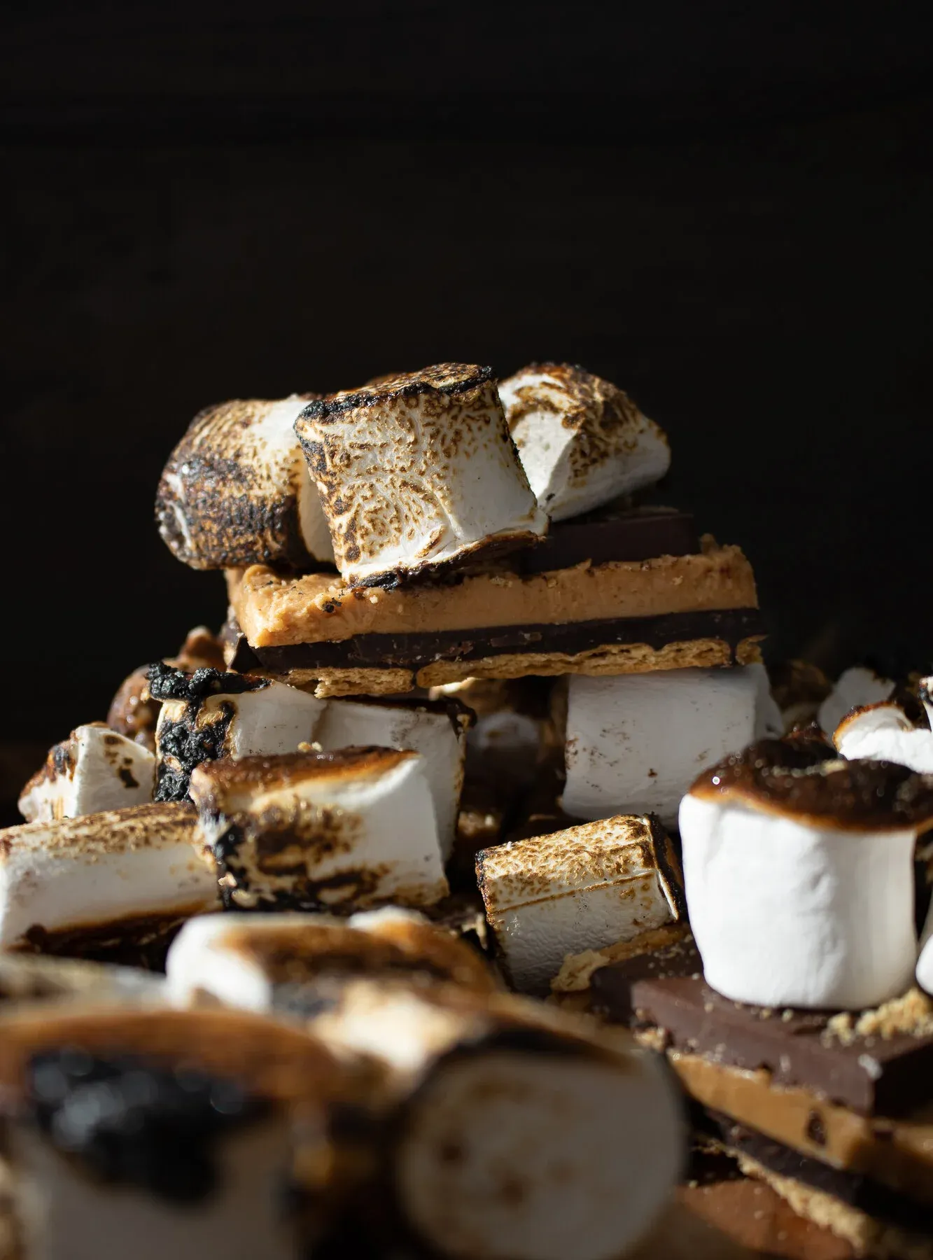 Moody close-up of a jumbled pile of No Bake Peanut Butter and Horchata S'mores Bars against a dark background