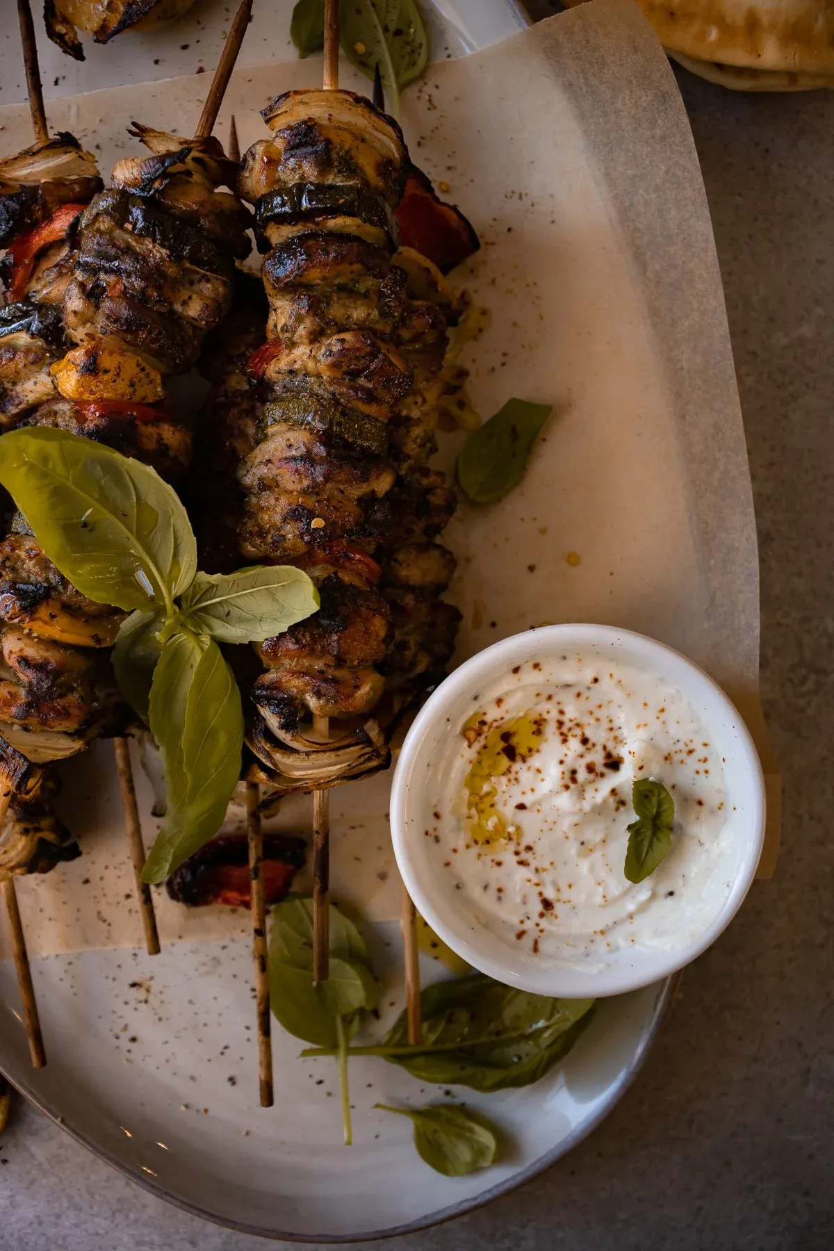 Angled overhead shot in moody lighting of the Grilled Chicken Skewers with Garlicky Whipped Ricotta on a white oval platter