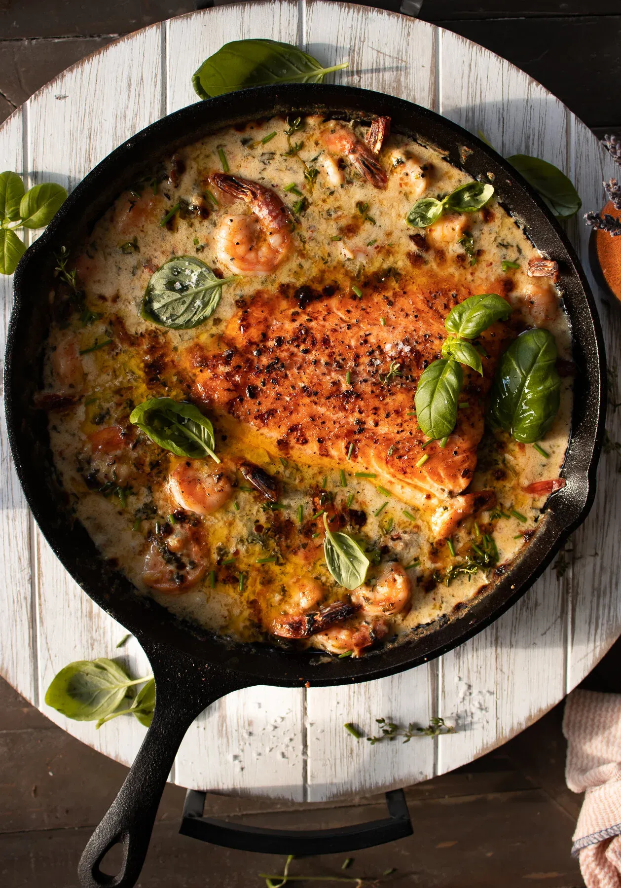 Full overhead view of the entire cast iron skillet of Saucy Salmon and Shrimp in Coconut Milk on a white plank board with bright sunlight streaming from the upper left