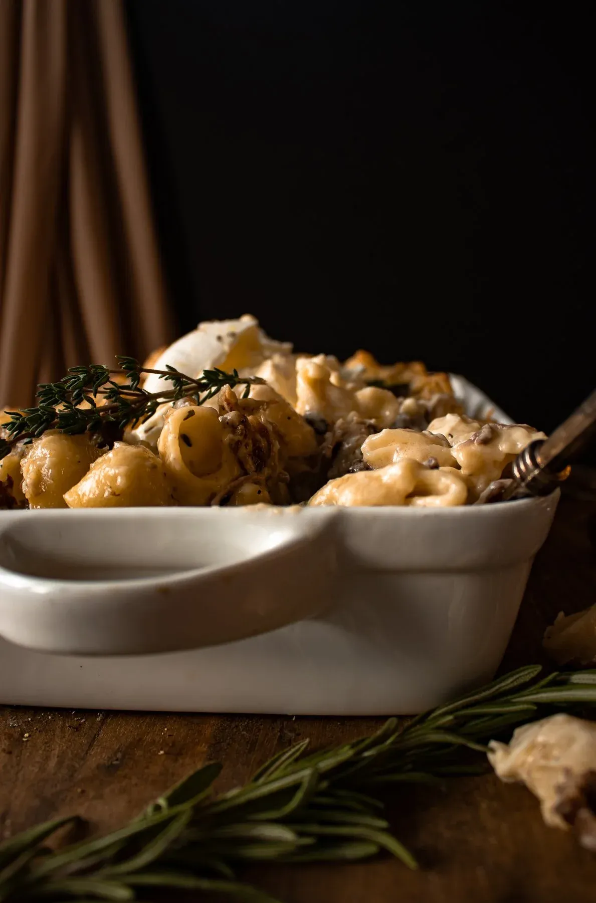Side-angle view of Short Rib Beecher's Mac and Cheese with Burrata in a white rectangular ceramic baking dish against a dark background