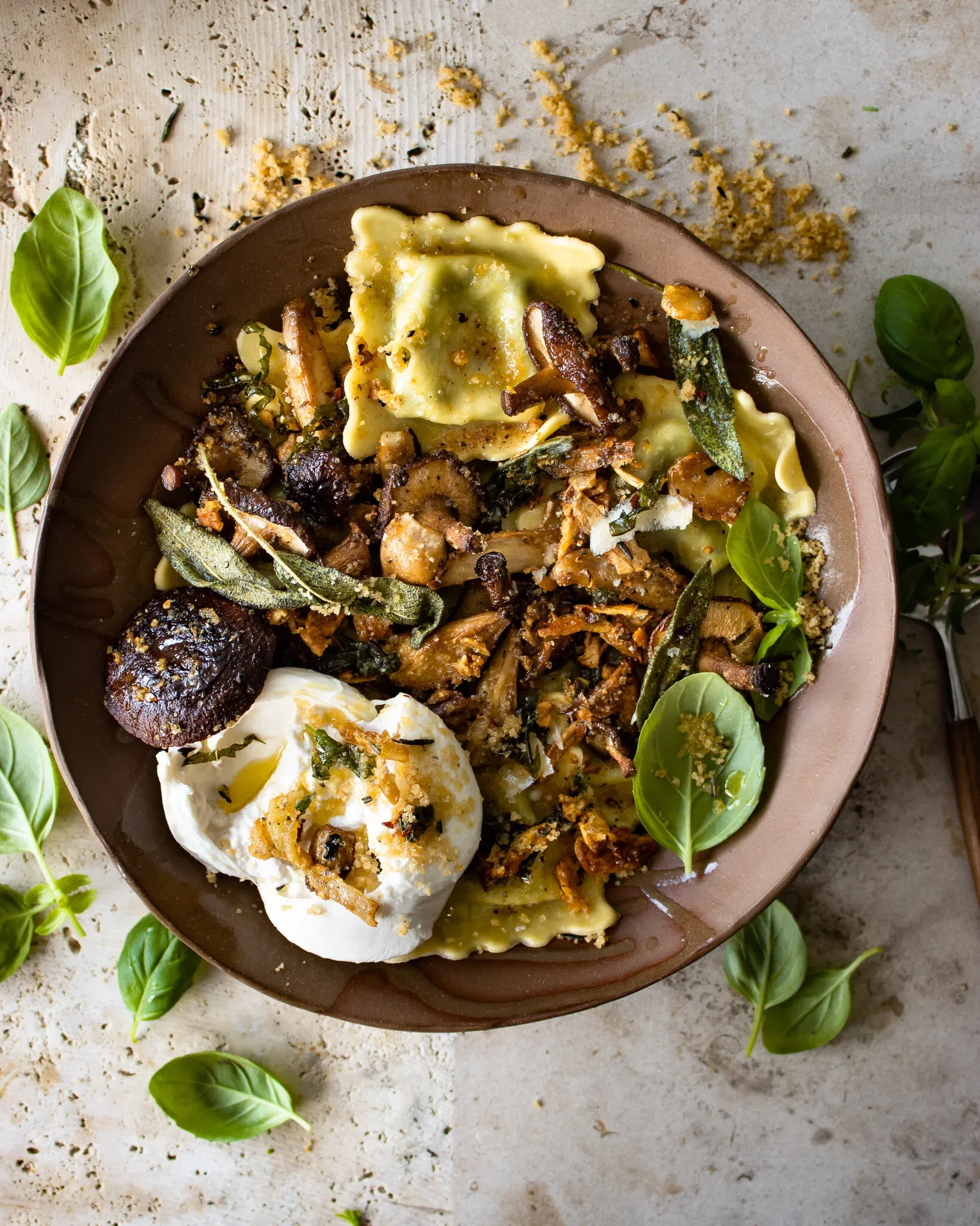 Overhead shot of the complete ravioli with sage and fried garlic butter sauce and roasted mushrooms in a dark brown ceramic bowl