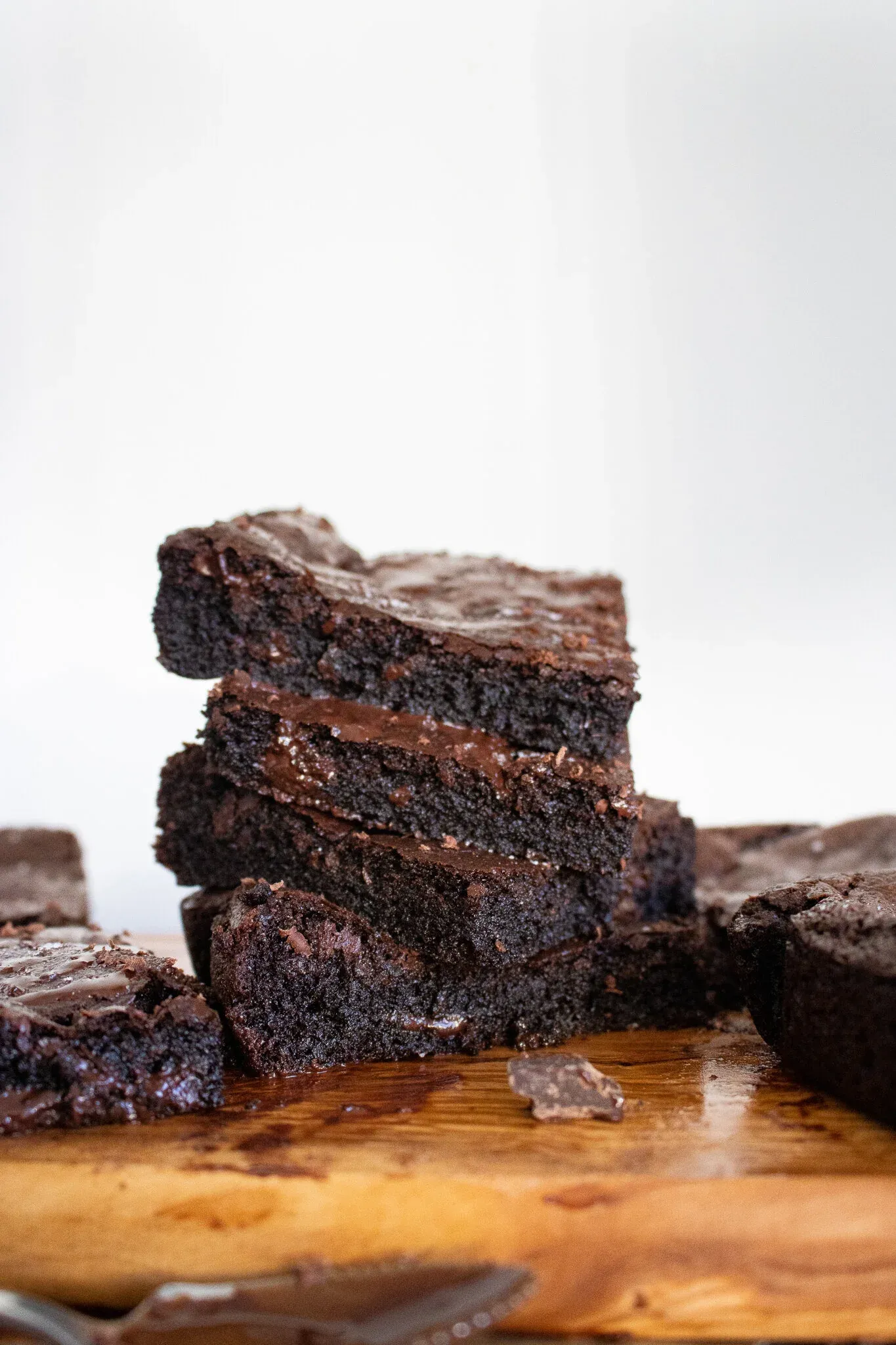 Side-angle view of four Vegan Dark Chocolate Brownies stacked slightly askew on a wood cutting board