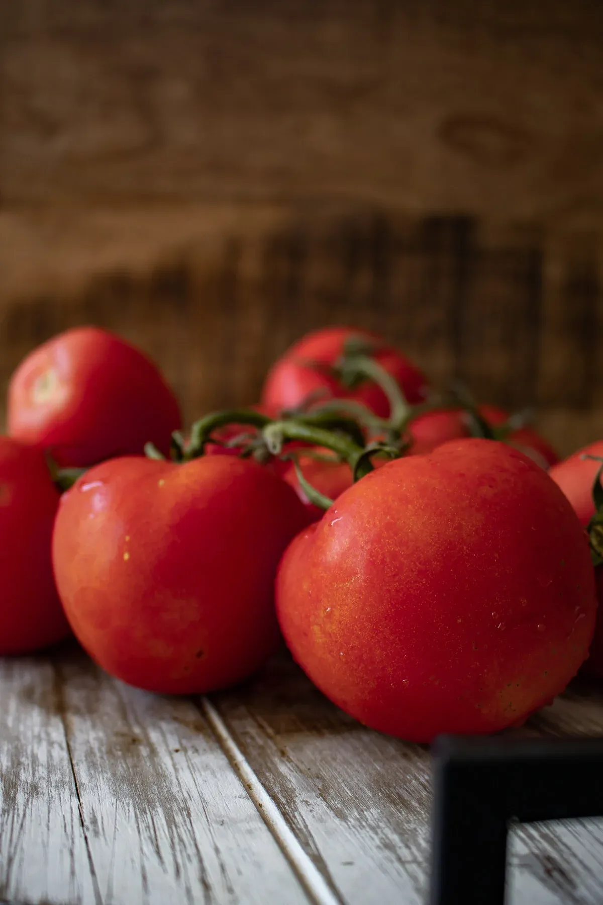 Fresh whole vine-ripened tomatoes clustered on a whitewashed wooden cutting board against a warm dark wood background