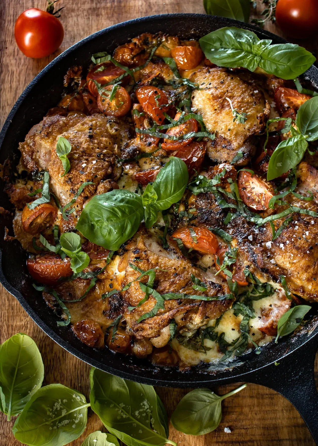 Elevated angled view of cast iron caprese chicken thighs in the cast iron skillet, looking slightly from the side