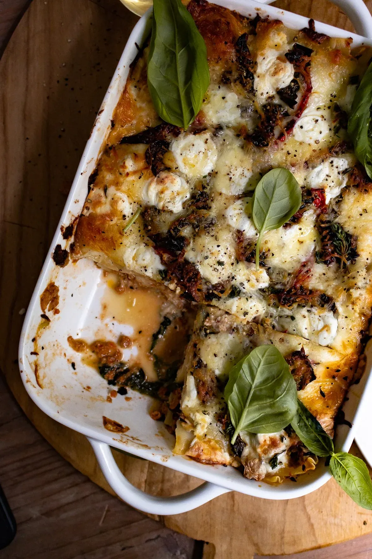 Angled overhead view of Spicy Chicken and Spinach Lasagna in a white ceramic baking dish with one corner serving removed