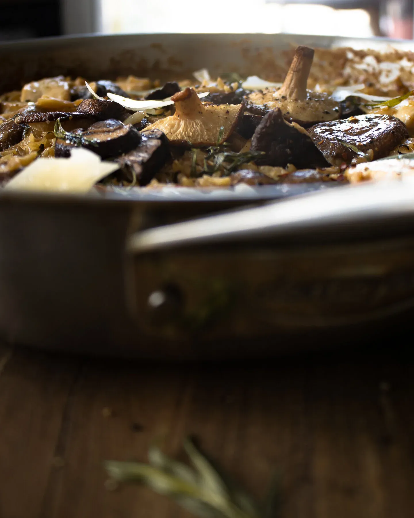Dramatic low-angle side shot of the stainless steel skillet rim framing deeply caramelized cremini and oyster-style mushrooms nestled in creamy orzo