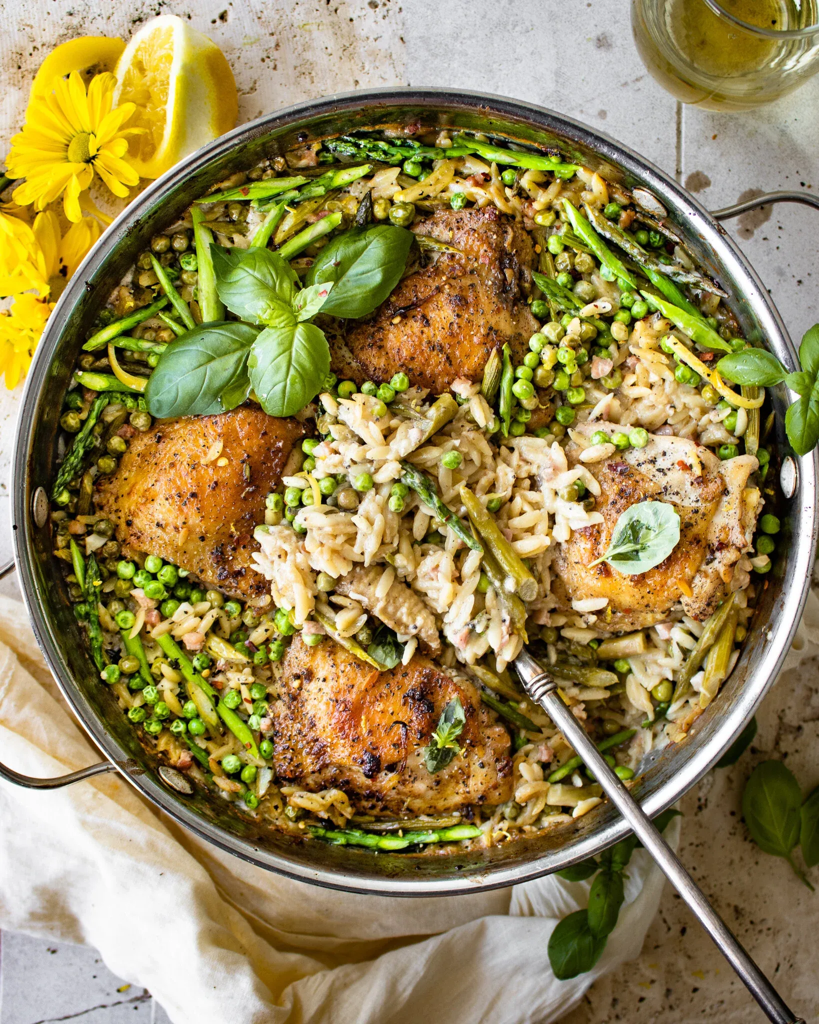 Overhead shot of the complete one-skillet chicken and spring vegetable orzo dish with a metal serving spoon resting in the center
