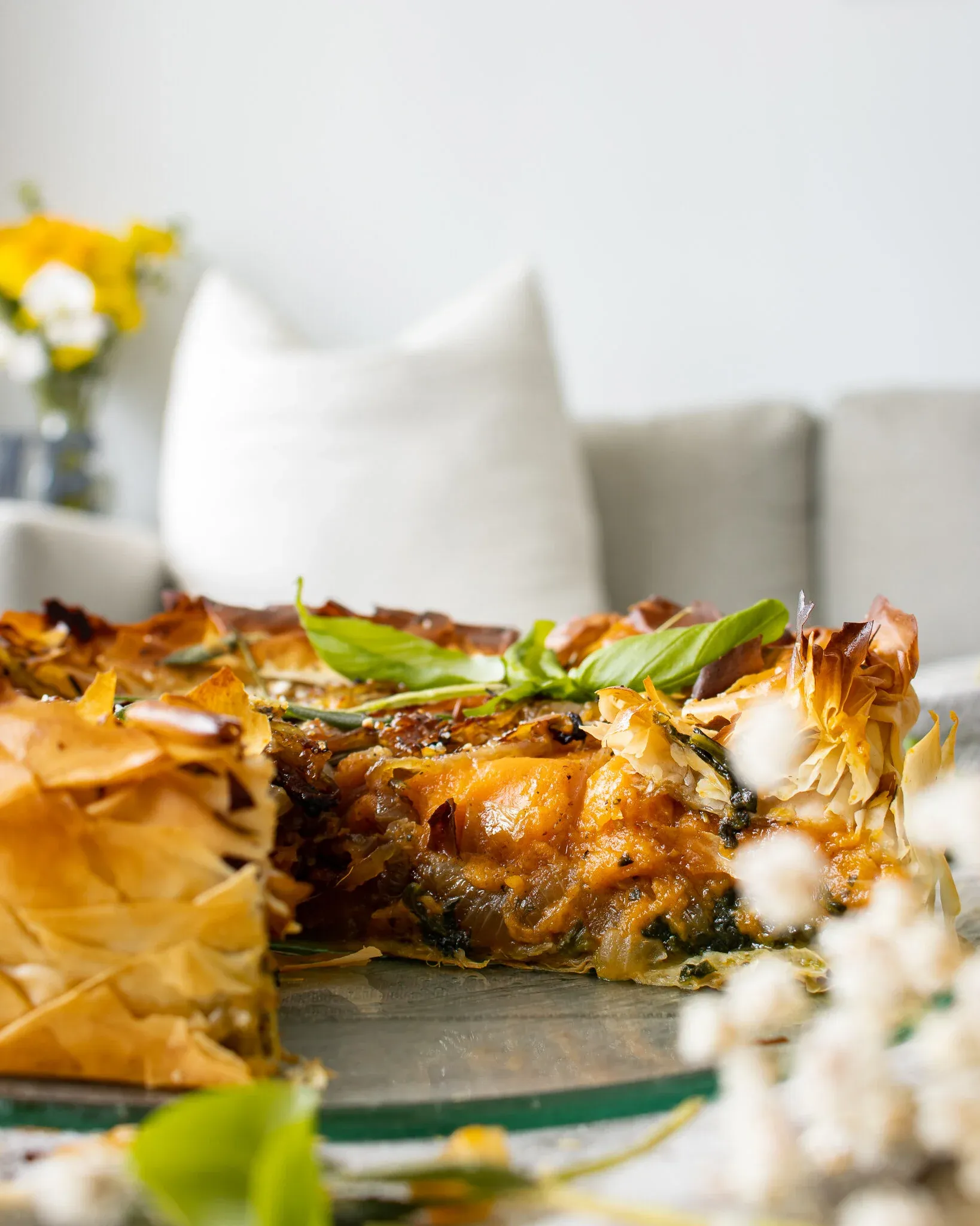 Side-angle view of the sweet potato, spinach and caramelized onion phyllo pie with one slice removed on a silver cake stand
